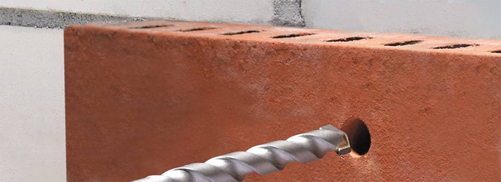 Ein Bohrer dringt in einen roten Ziegelstein ein, um ein Loch für Befestigungen oder Installationen zu schaffen.