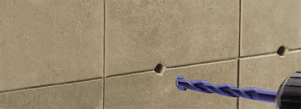 Ein Bohrer bohrt ein Loch in eine Fliesenwand. Die Wand hat eine hellbraune Farbe mit quadratischen Fliesen, die durch Fugen getrennt sind.