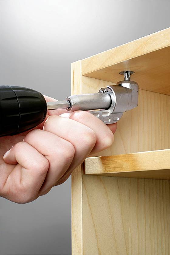 Eine Hand verwendet einen Akkuschrauber, um ein Scharnier an einem Holzmöbel zu befestigen.
