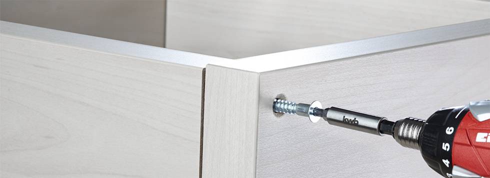 Ein Akkubohrer befestigt eine Schraube in einem hellen Holzmöbel, zeigt eine Schritt-für-Schritt-Anleitung zur Möbelmontage.