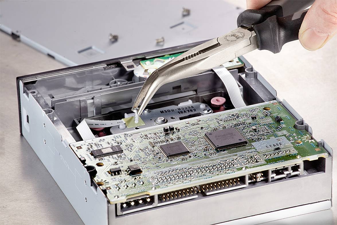 Eine Hand hält eine Pinzette und arbeitet an einer offenen Computerfestplatte. Die Platine und elektronische Bauteile sind sichtbar.