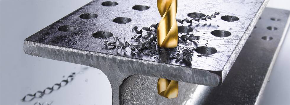 Ein Bohrer durchdringt eine Metallplatte mit Löchern, umgeben von Metallspänen.