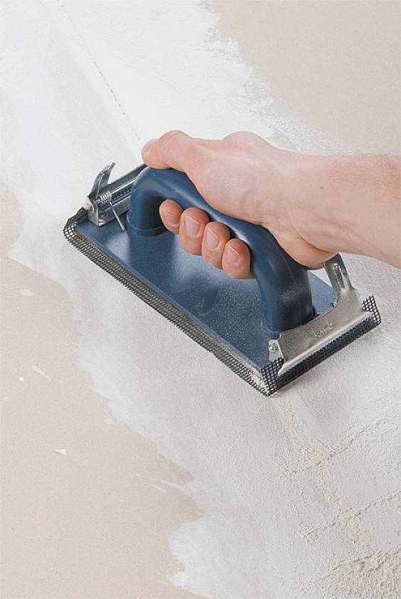 Hand schleift eine verputzte Wand mit einem Schleifblock ab, um die Oberfläche zu glätten.