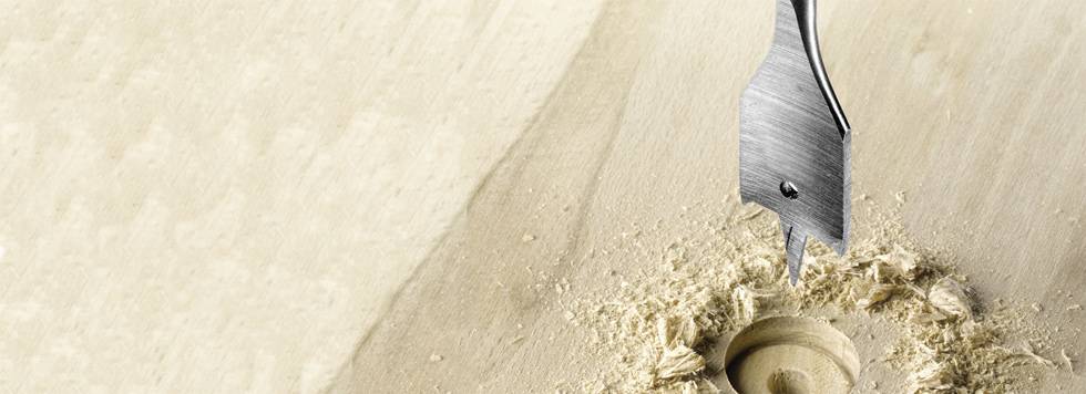 Nahaufnahme eines Bohrers, der ein Loch in ein Holzbrett bohrt, mit Holzspänen um das Loch.