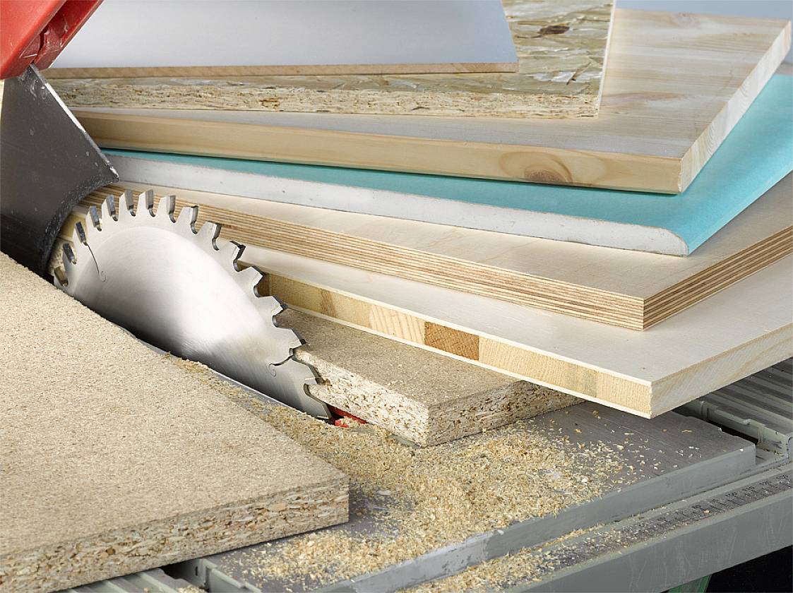 Ein Sägeblatt schneidet durch mehrere Holzplatten unterschiedlicher Dicke. Holzspäne bedecken die Fläche um die Säge.