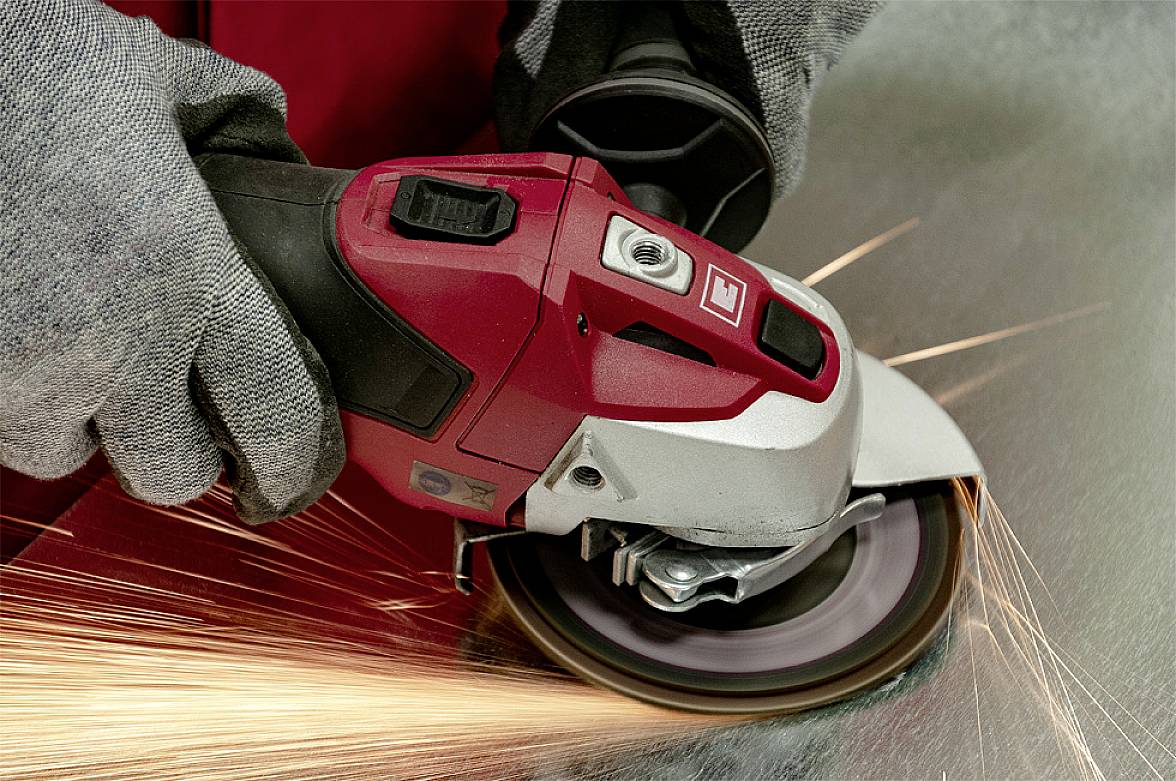 Eine Person schleift eine Metalloberfläche mit einem Winkelschleifer. Funken sprühen vom Kontaktpunkt.