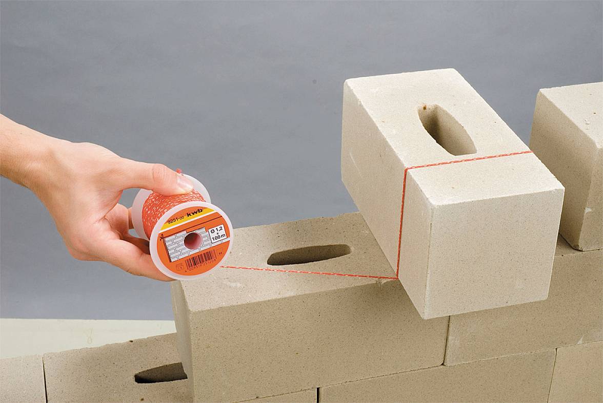 Eine Hand hält eine Rolle mit Mauerwerks-Schnur, die über gestapelte Lochziegel gespannt ist.