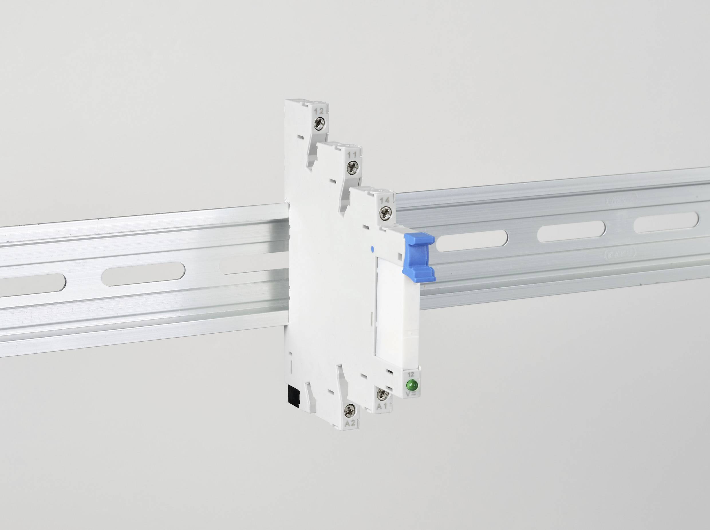 Ein weißer elektrischer Schalter, montiert auf einer silbernen Hutschiene, mit einem blauen Hebel und einem grünen Knopf vorne.