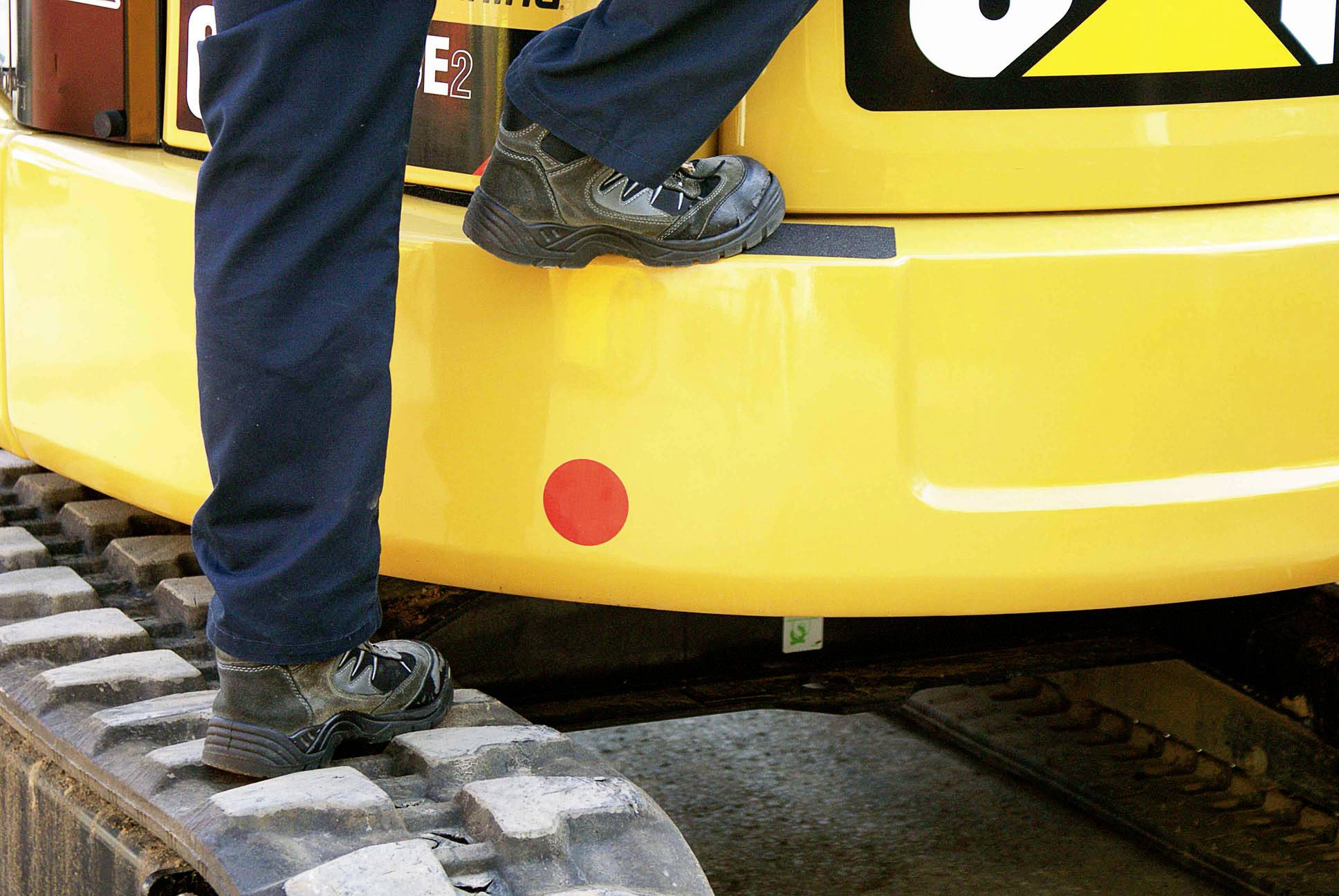 Eine Person steigt in einen gelben Bagger, sichtbar sind nur die Beine auf den Kettengliedern.