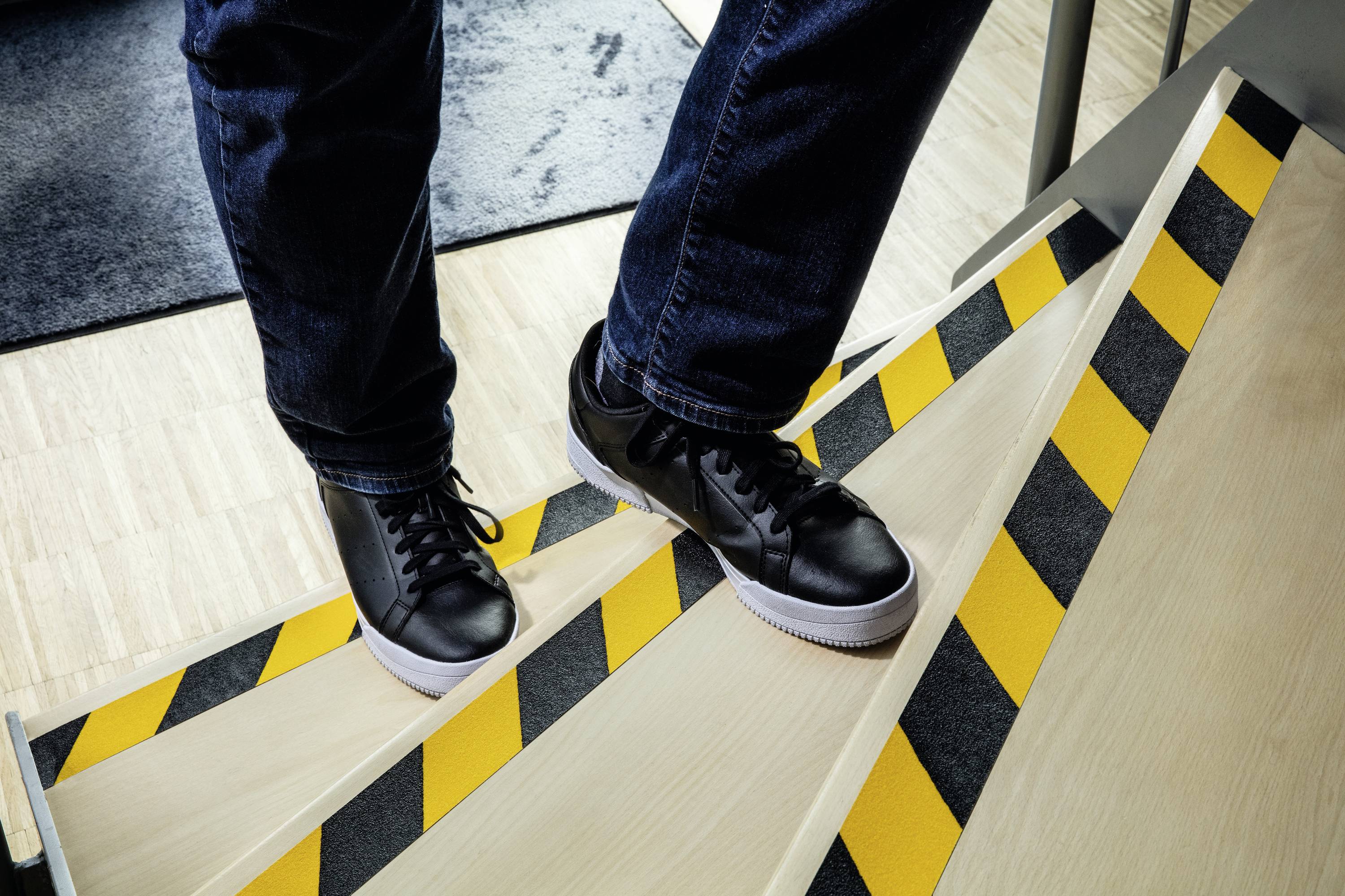 Person steigt mit Turnschuhen eine Treppe mit schwarz-gelben Warnstreifen hinunter.