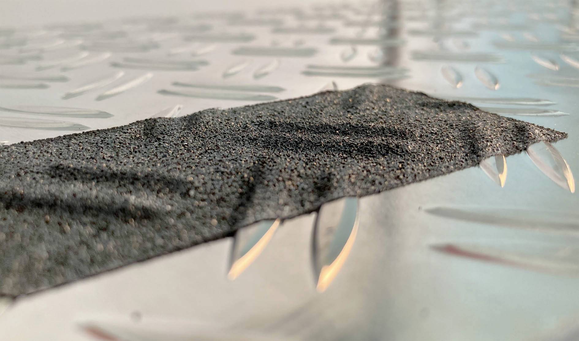 Nahaufnahme eines rechteckigen, rutschfesten Streifens auf einer metallischen Oberfläche. Der Streifen hat eine raue Textur.