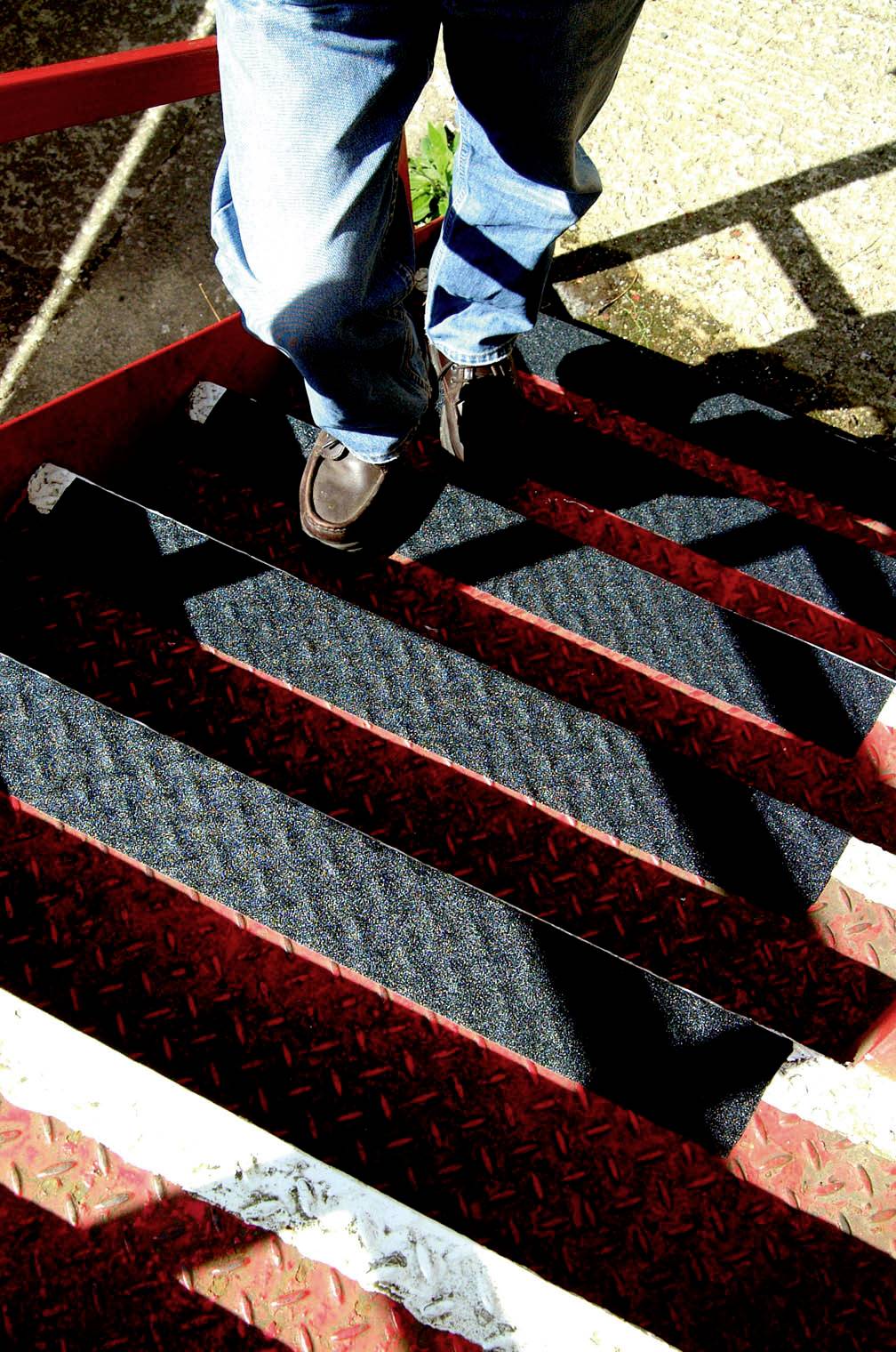 Person in Jeans und braunen Schuhen geht eine rot-schwarze Treppe hinunter.