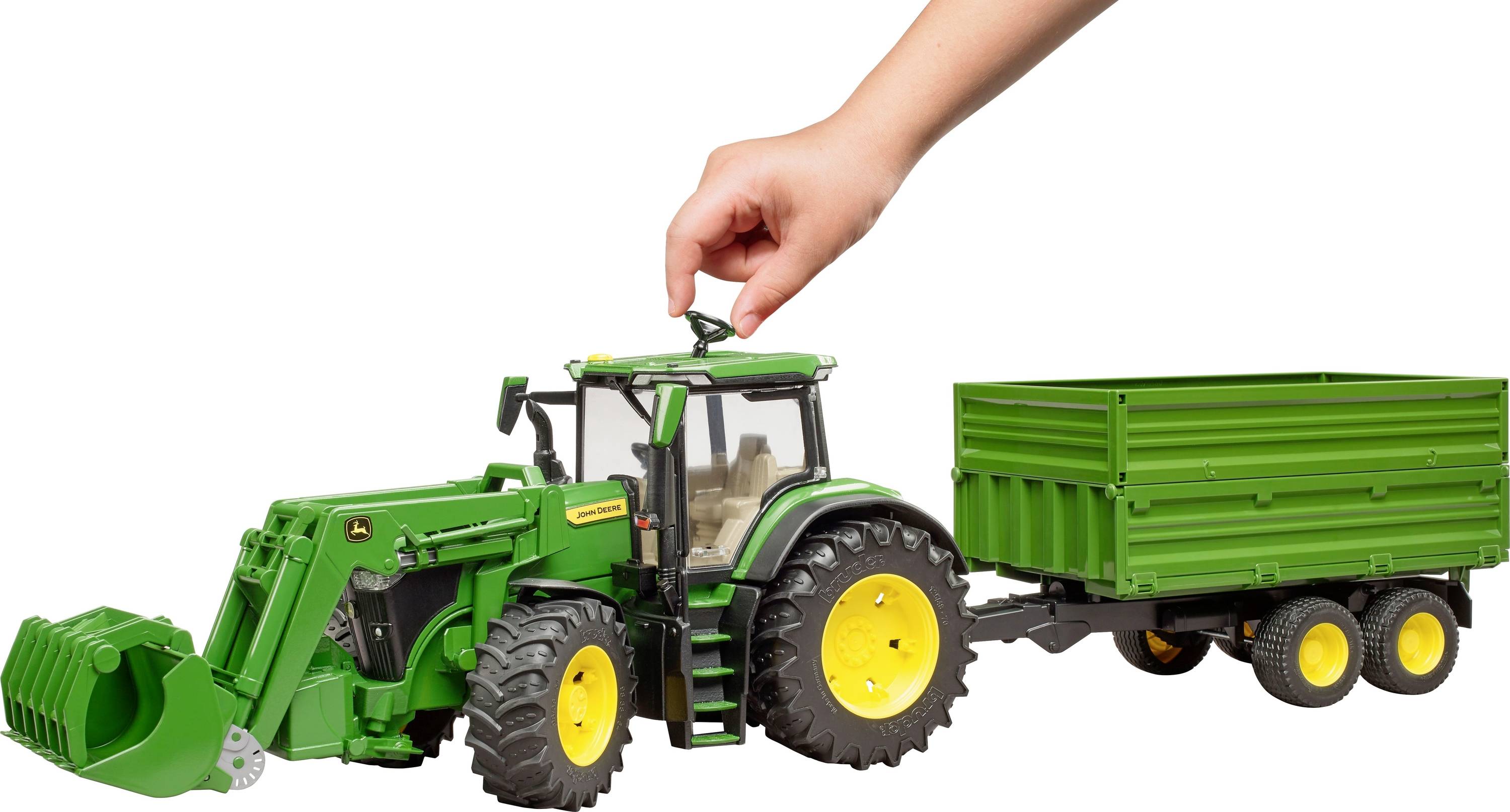 Eine Hand hebt ein Spielzeugtraktor mit Anhänger an.