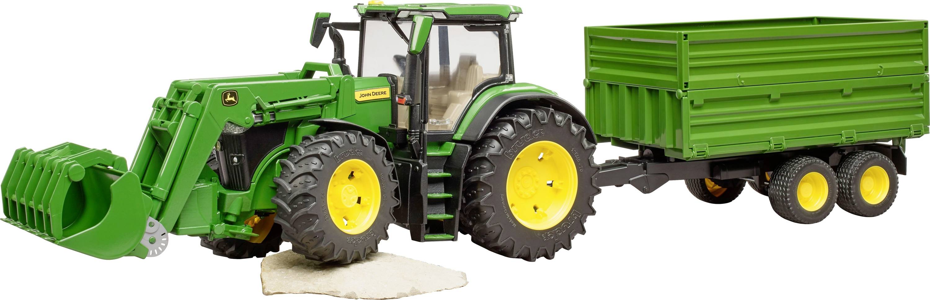 Grüner Spielzeugtraktor mit Anhänger, steht auf weißem Untergrund. Traktor hebt helle Platte mit Vorderradschaufel an.