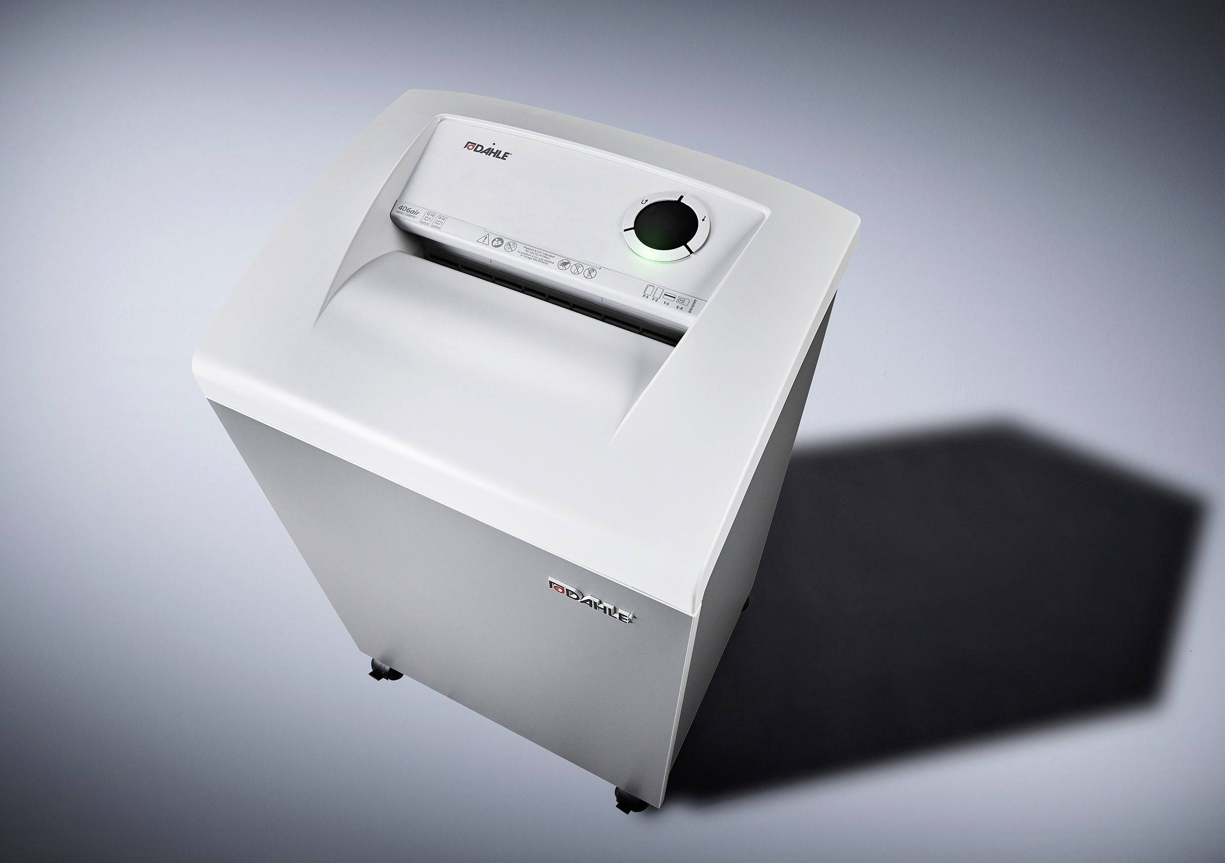 Grau-weißer Büroschredder auf einem dunklen Hintergrund, zeigt den Einzugsschlitz und Bedienknopf oben, auf Rollen stehend.