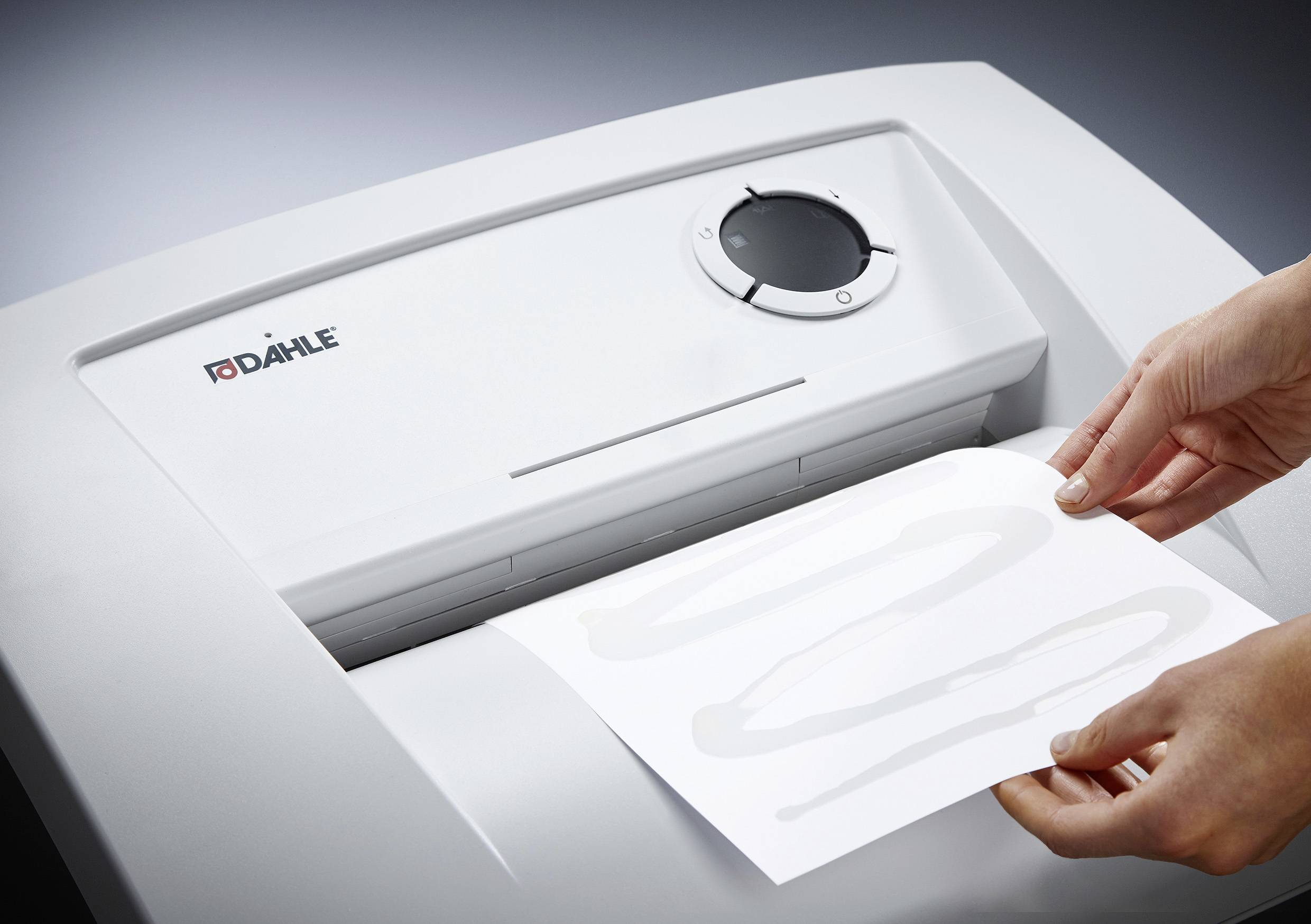 Eine Person führt ein Blatt Papier in einen Aktenvernichter ein. Das Gerät ist von der Marke Dahle und hat ein Kontrollrad für Einstellungen.