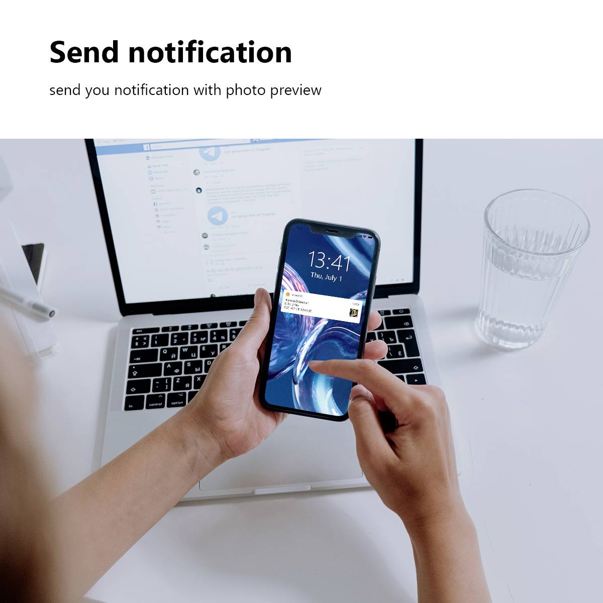 Eine Person hält ein Smartphone mit einer Benachrichtigung über ein neues Bild, während im Hintergrund ein Laptop zu sehen ist.