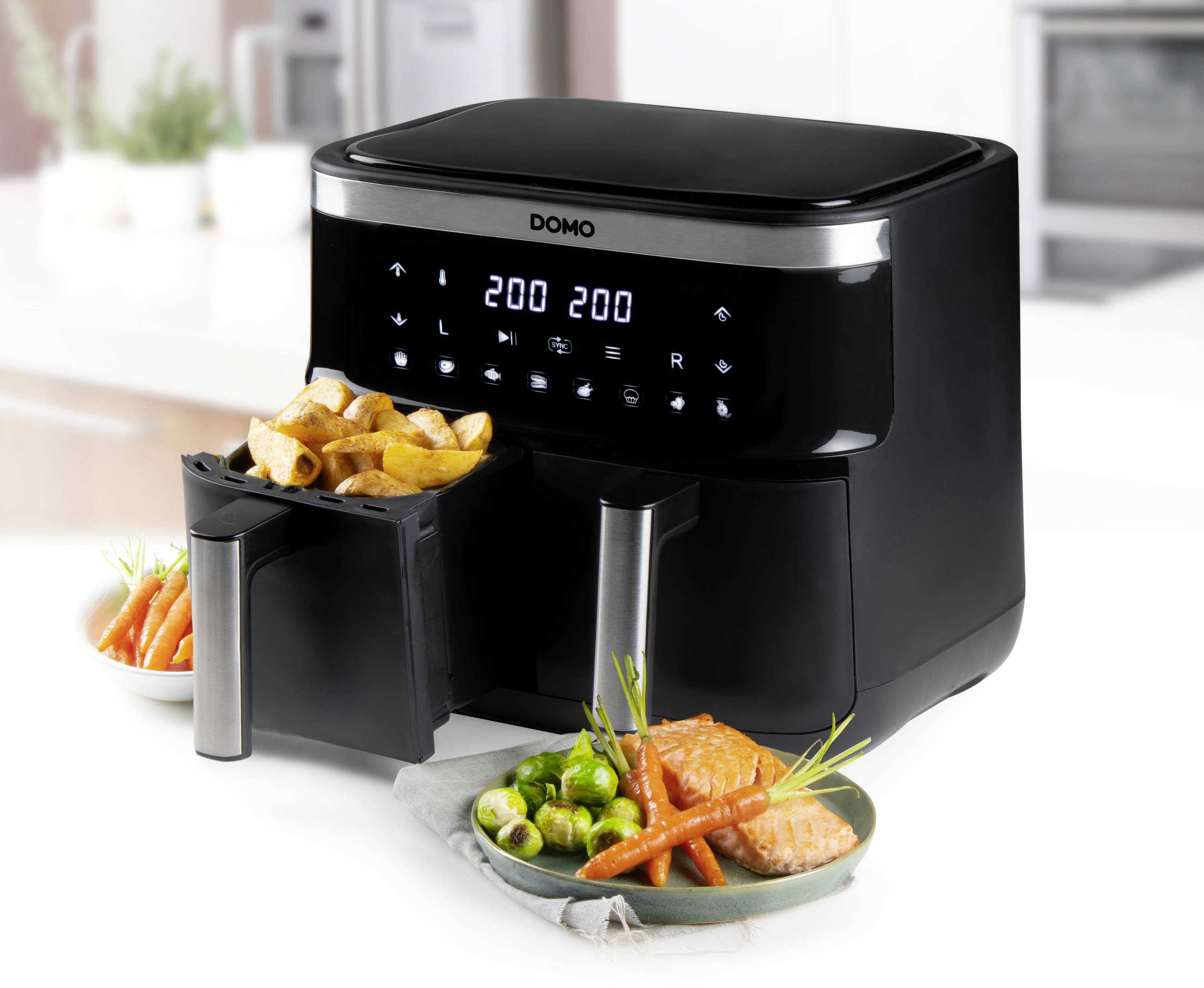 Schwarze Heißluftfritteuse mit digitaler Anzeige, zeigt '200' Grad Celsius. Zwei Tabletts, eines gefüllt mit Pommes, das andere mit Lachs, Karotten und Rosenkohl.