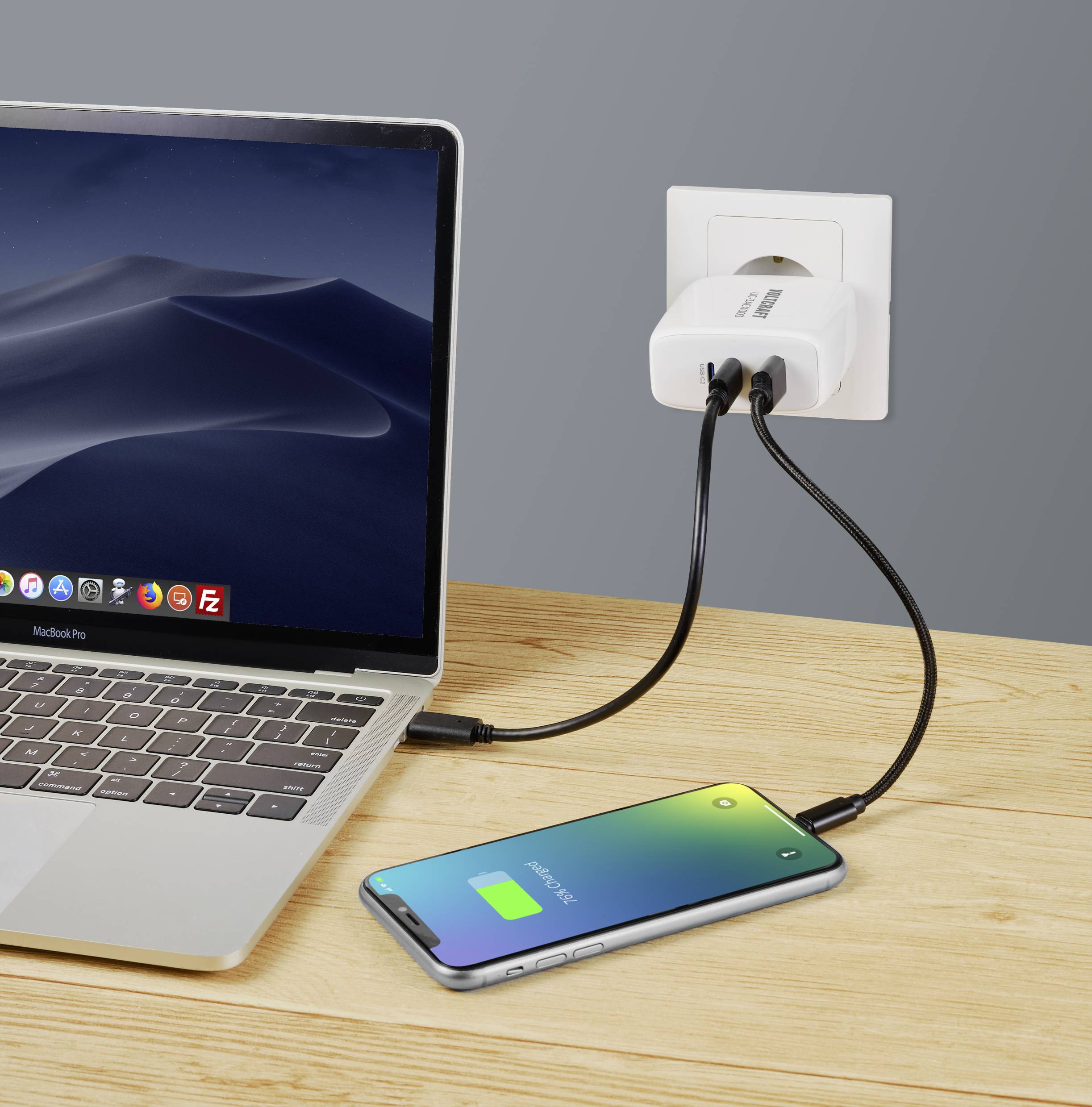 Laptop und Smartphone auf einem Holztisch. Beide Geräte sind über ein Ladegerät an einer Steckdose angeschlossen. смартфон zeigt grünen Akku.
