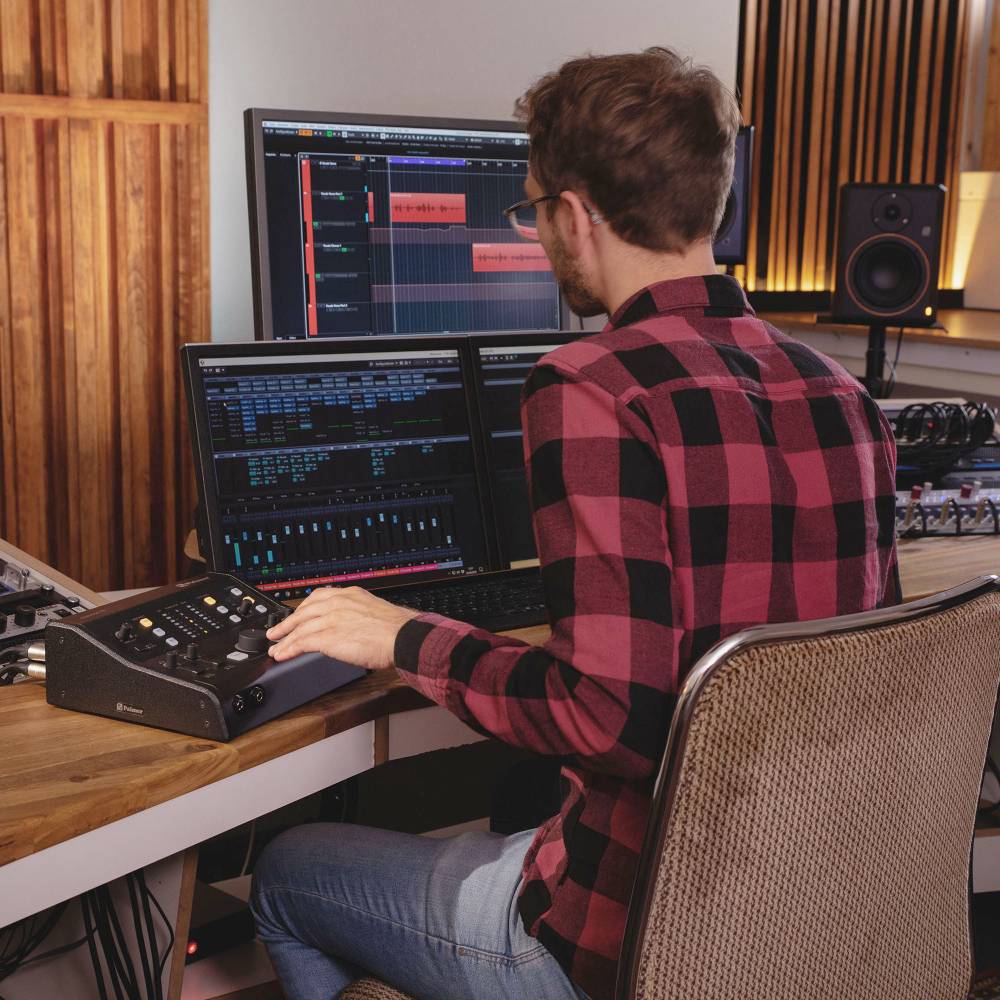 Eine Person mit Kopfhörern arbeitet an einem Computer mit Audiobearbeitungssoftware in einem Tonstudio.