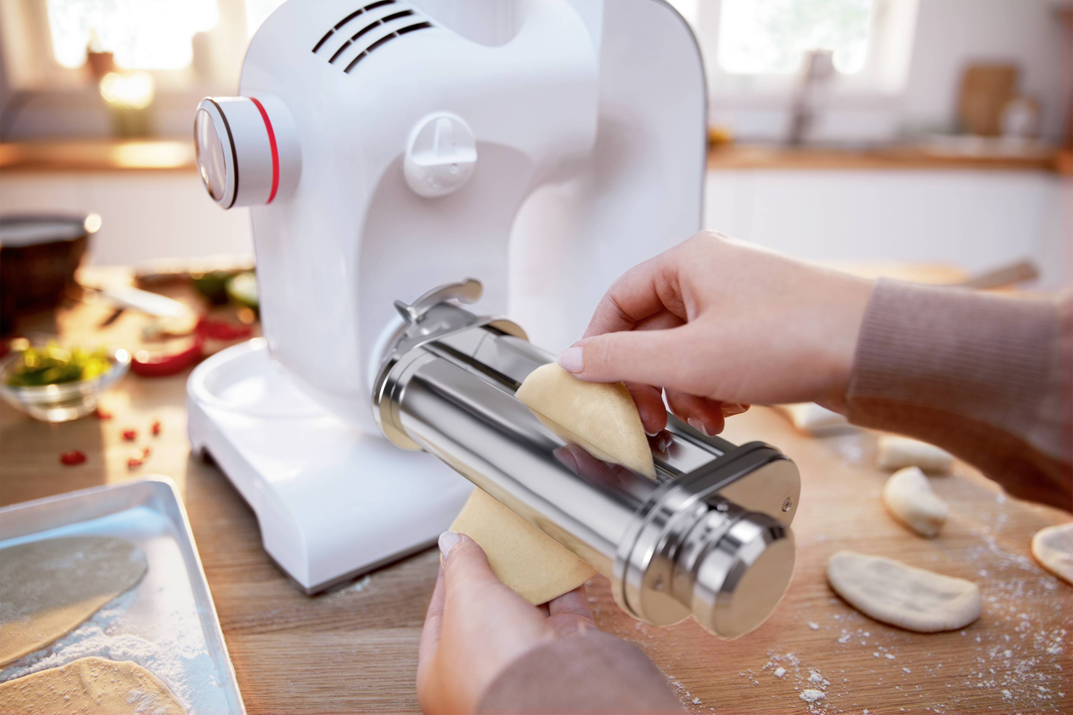 Person formt Teig mit einer Küchenmaschine auf einer Arbeitsfläche. Umgebung zeigt Zutaten und fertige Teigstücke.