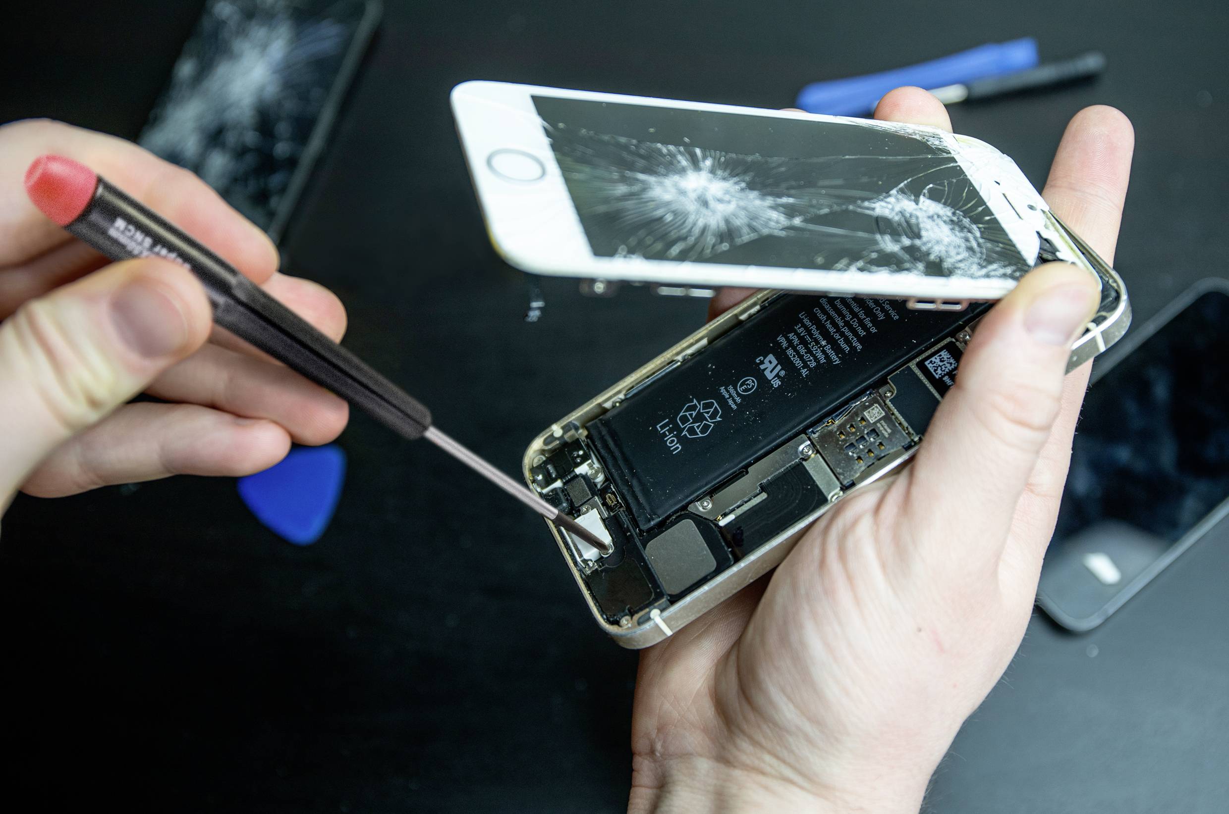 Person hält ein Smartphone mit gesprungenem Bildschirm, öffnet es mit Werkzeug, um Innenkomponenten zu zeigen. Reparaturszene.