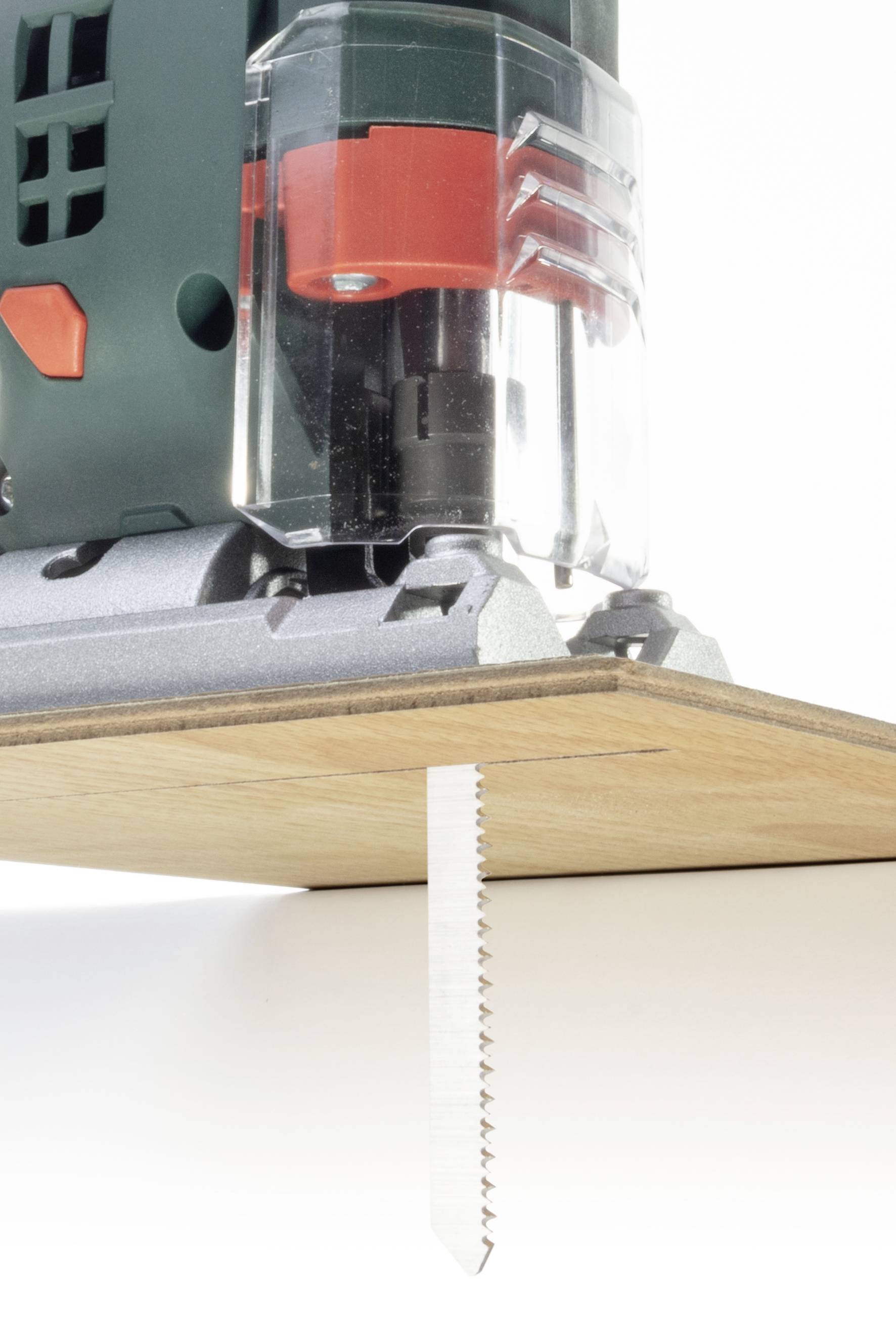 Elektrische Stichsäge schneidet Holzplatte. Zeigt das Sägeblatt in Aktion unterhalb der Platte.