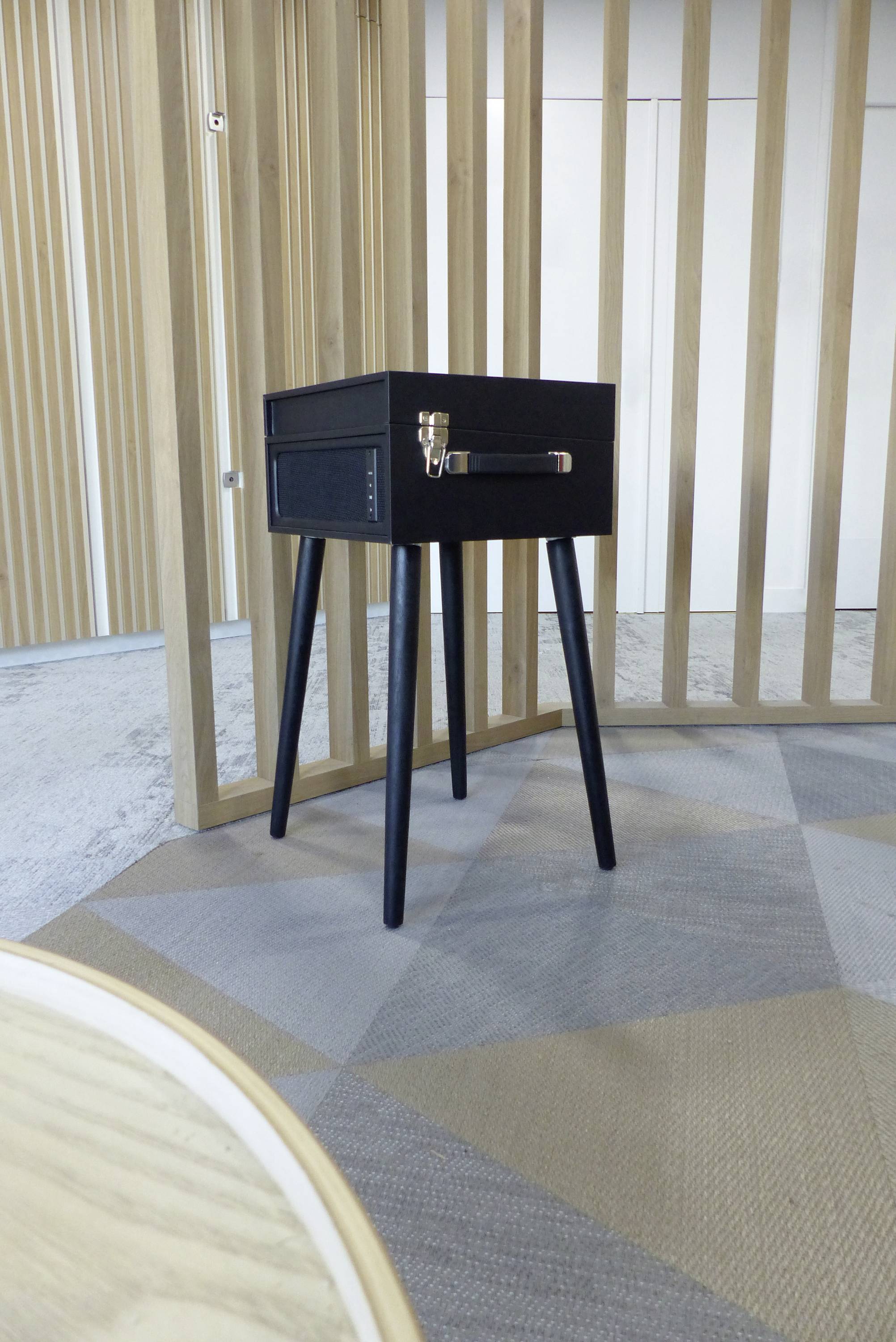 Ein schwarzer, quadratischer Tisch mit vier Beinen steht auf einem stilvollen Teppich in einem modern eingerichteten Raum mit Holzelementen.