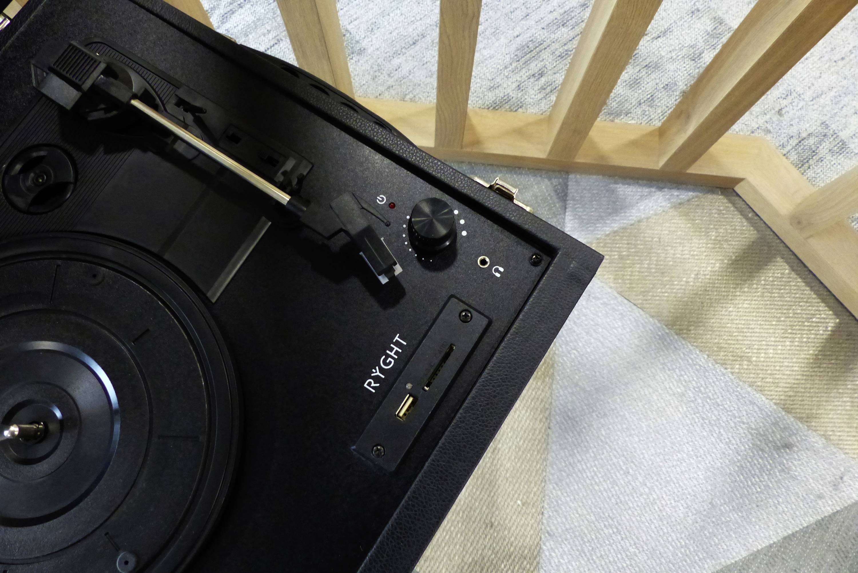 Ein schwarzer Plattenspieler auf einem hellen Teppich neben einem Holzgitter.