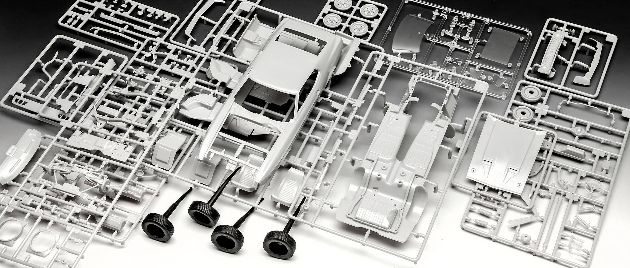 Bauteile eines Modellauto-Bausatzes aus Kunststoff zeigen Karosserie, Reifen und Zubehörteile. Die Teile sind ungeordnet angeordnet.