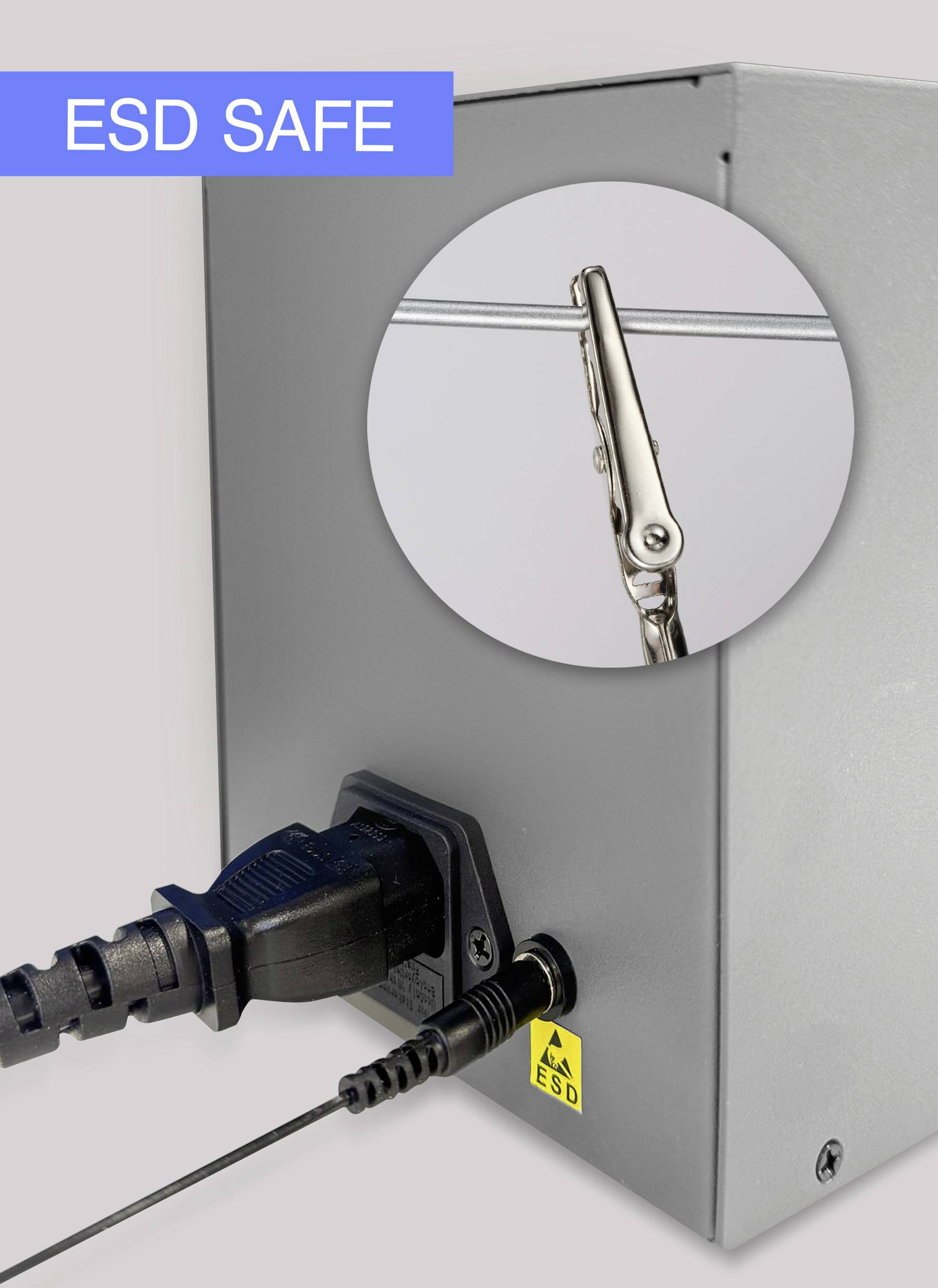 Ein silbernes Gerät mit Kabelanschlüssen. Ein Kreisfenster hebt eine Krokodilklemme hervor. Oben links steht 'ESD SAFE'.