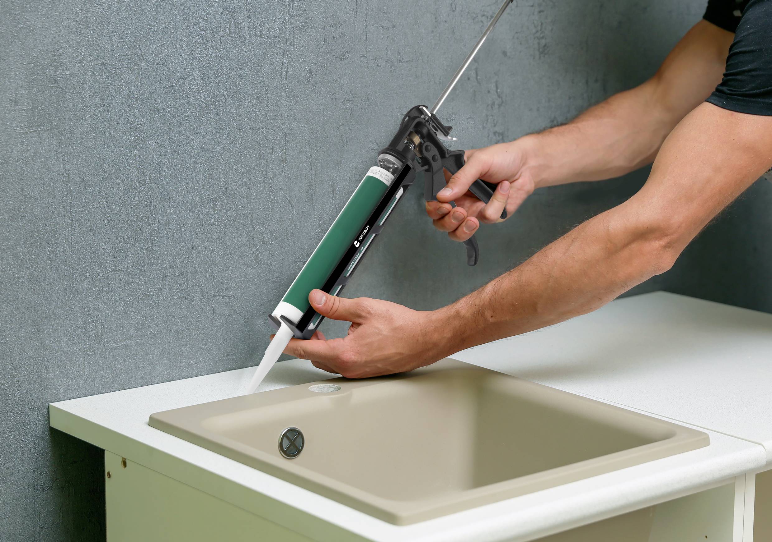 Eine Person verwendet eine Kartuschenpistole, um Dichtmittel um ein Waschbecken aufzutragen. Hände halten die Pistole über dem Rand des Beckens.