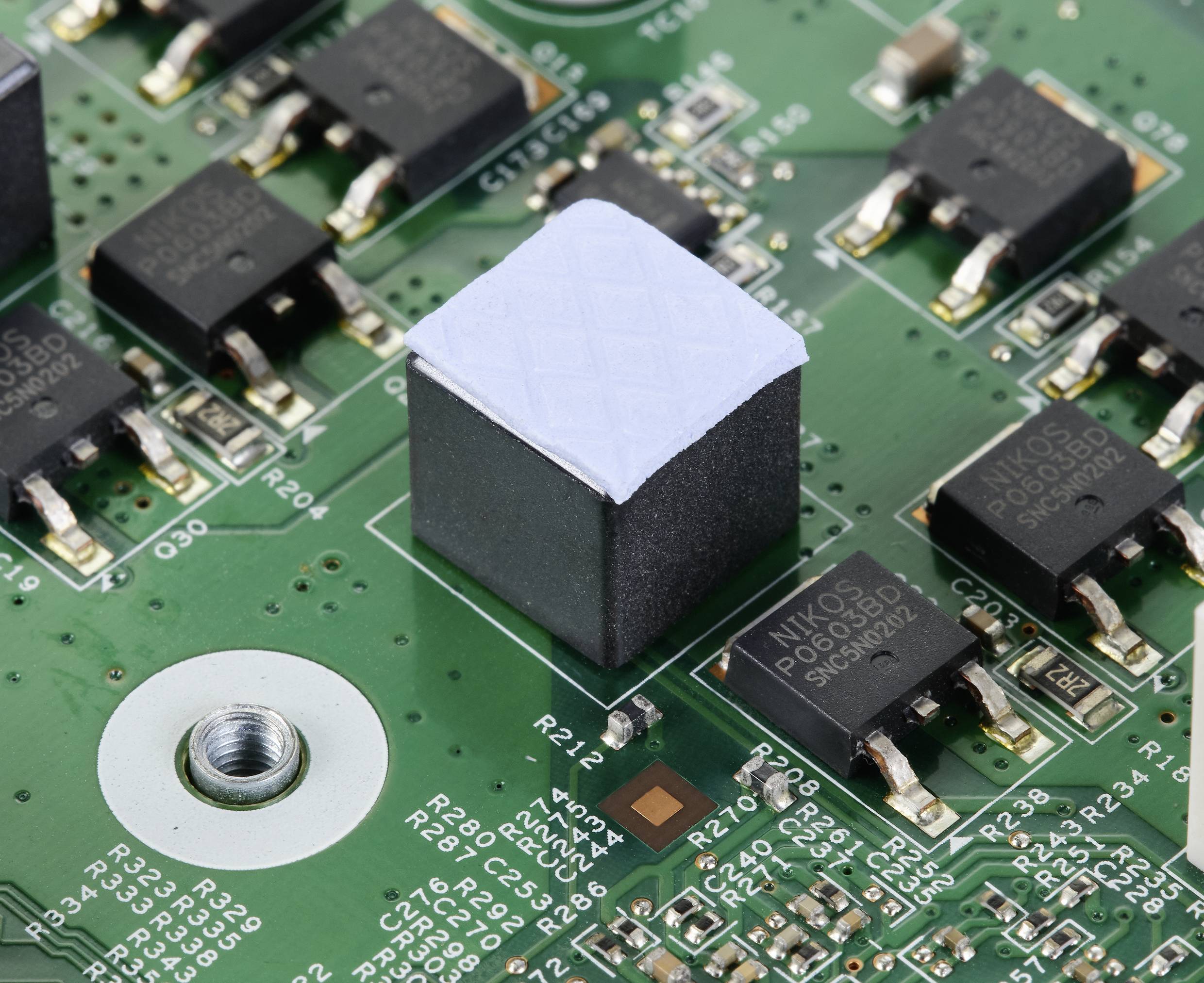 Nahaufnahme einer grünen Leiterplatte mit mehreren schwarzen elektronischen Komponenten und einem zentralen, größerem quadratischen Bauelement.