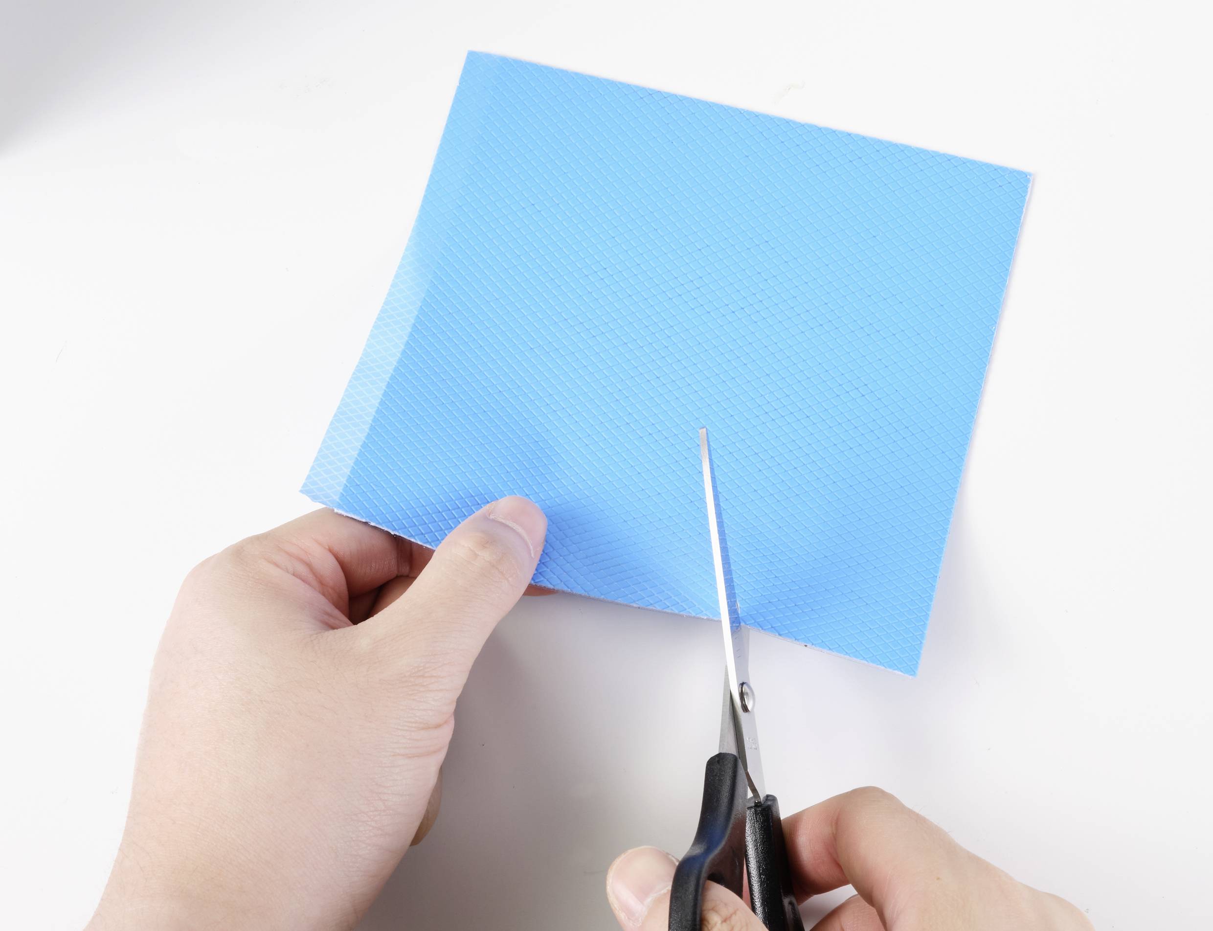 Person schneidet ein blaues Stück Papier mit einer Schere auf einem weißen Hintergrund.