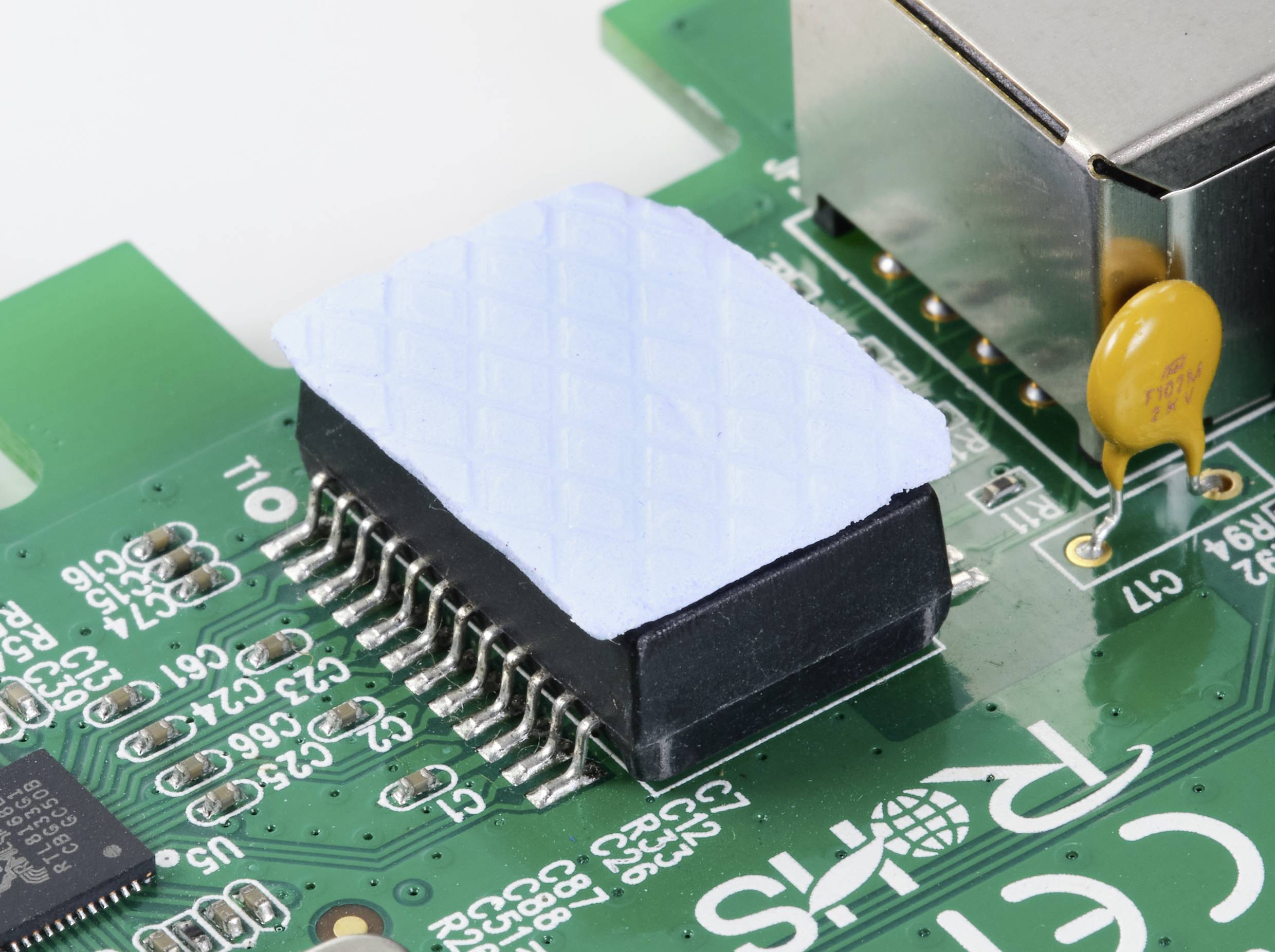 Eine Nahaufnahme einer grünen Leiterplatte mit einem integrierten Schaltkreis, teils von einem blauen Kühlpad abgedeckt.