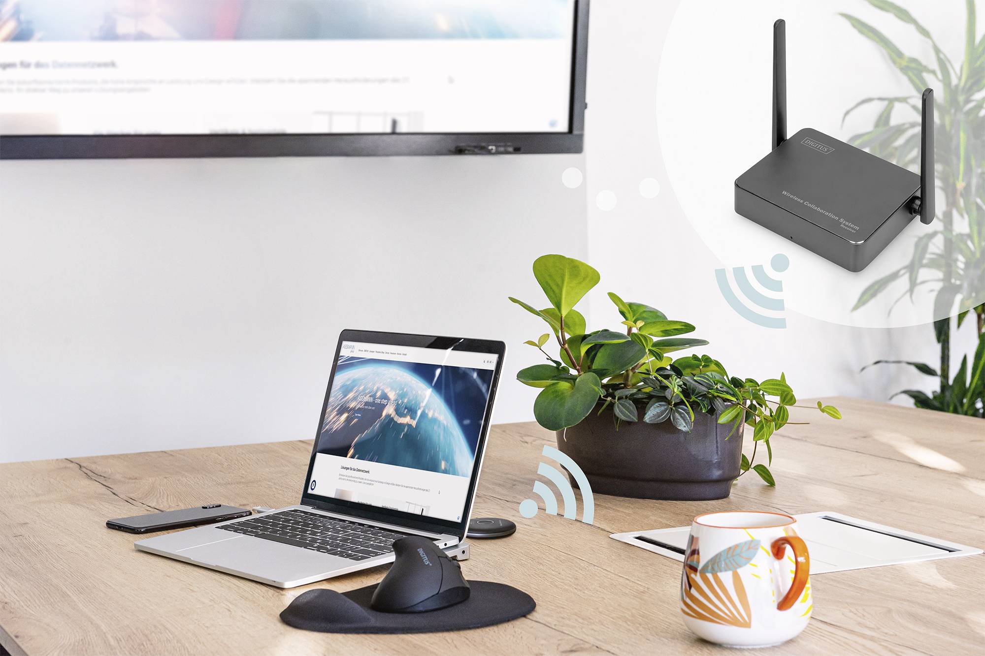 Ein Laptop auf einem Tisch zeigt eine Erde-Darstellung auf dem Bildschirm. Ein WLAN-Router sendet ein Signal. Im Hintergrund ein Monitor.