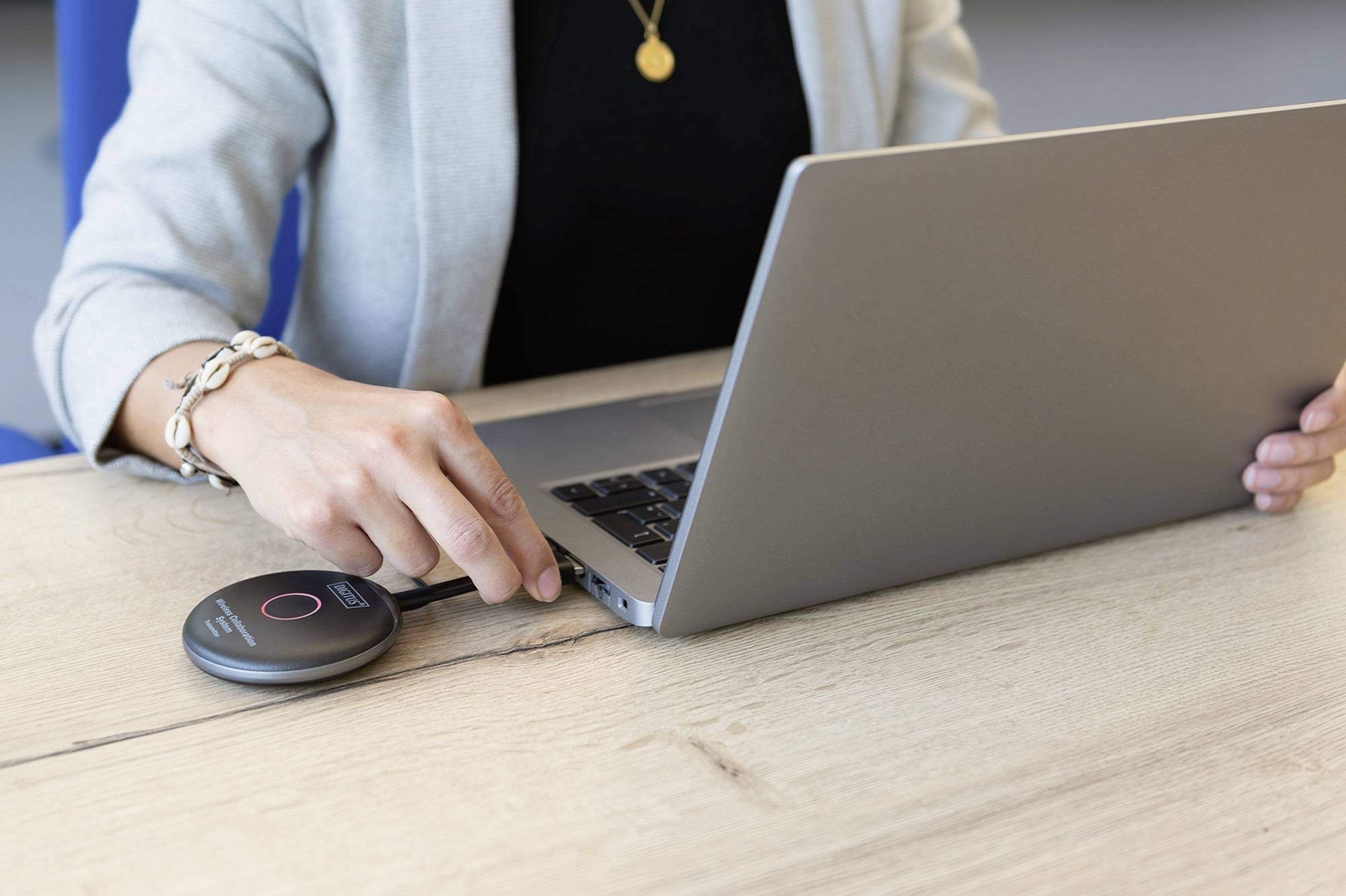 Eine Person verbindet ein tragbares Gerät mit einem Laptop über ein Kabel auf einem Holztisch.