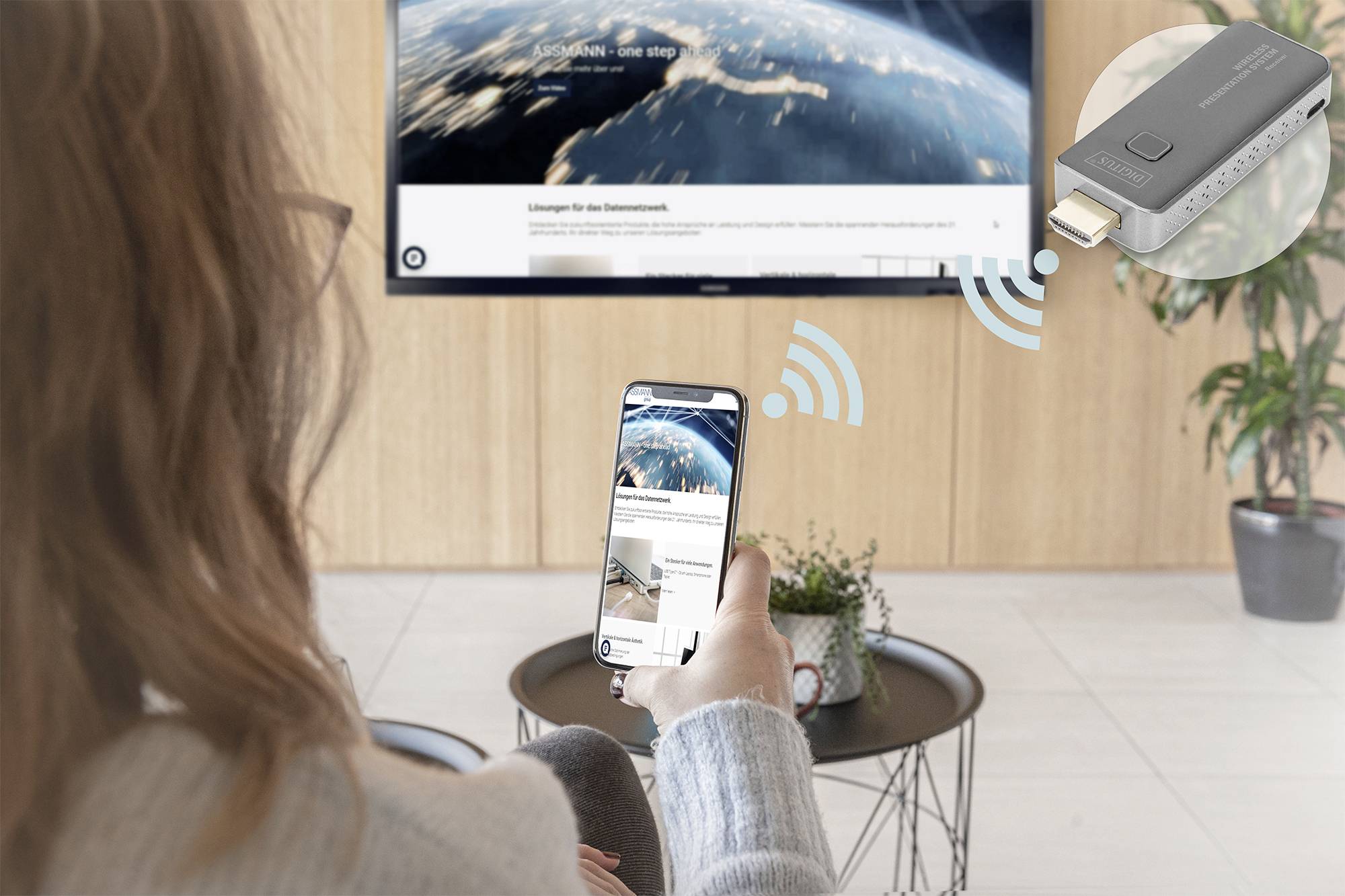 Eine Person mit Smartphone spiegelt Inhalte drahtlos auf einen Fernseher. Ein HDMI-Stick erscheint als Verbindungsmittel.