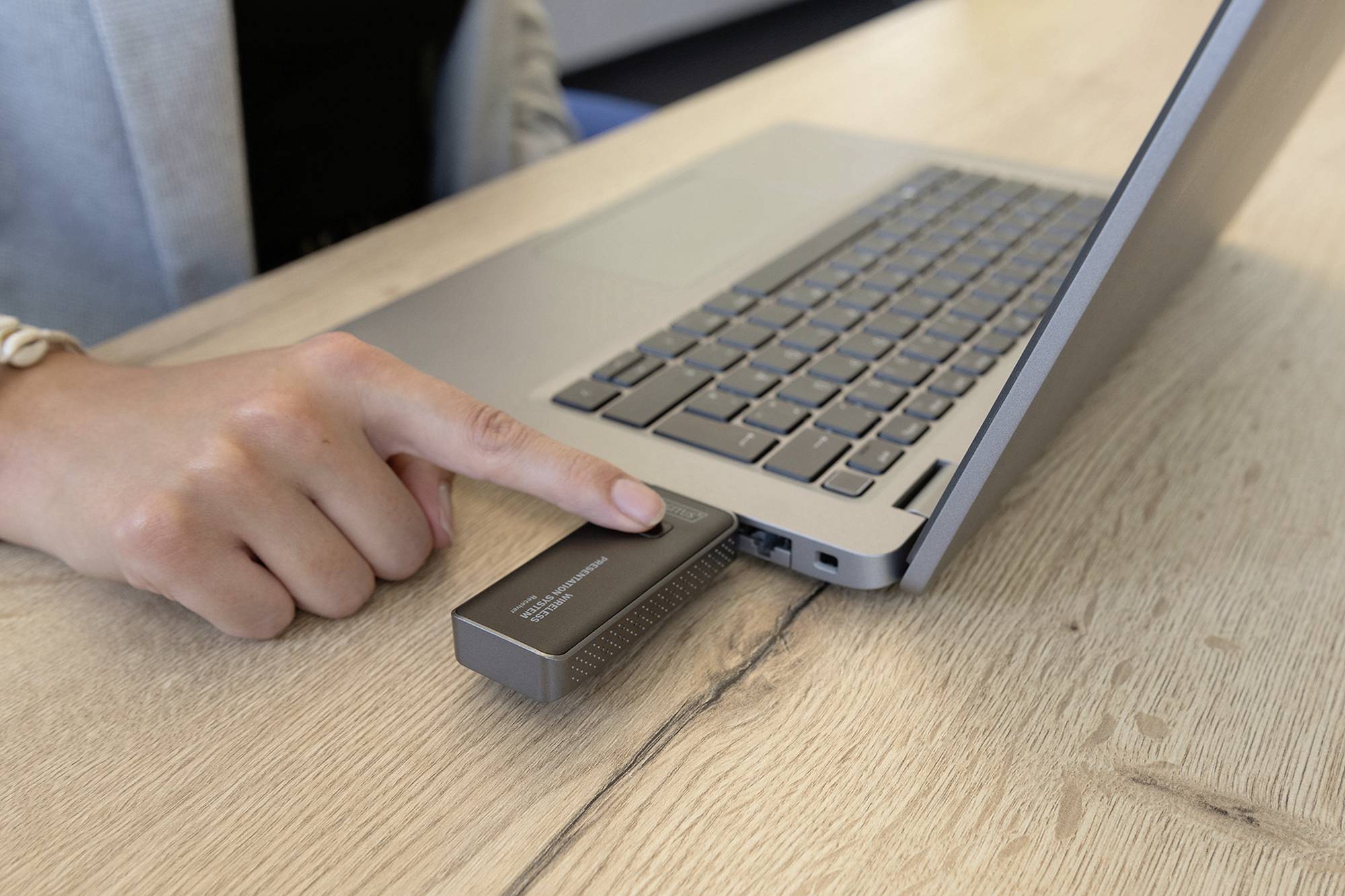 Eine Person verbindet ein externes Gerät über USB mit einem Laptop, um Daten zu übertragen. Das Gerät liegt auf einem Holztisch.