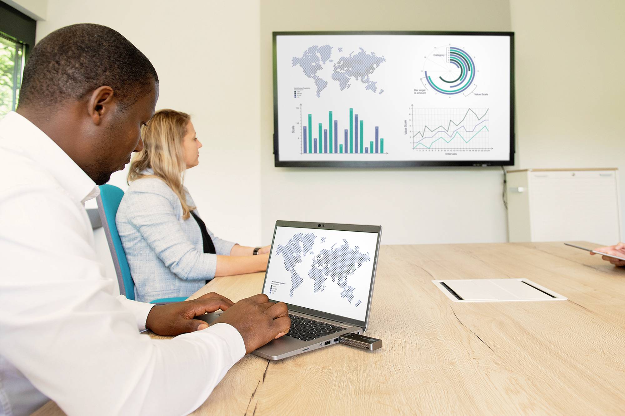 Zwei Personen im Konferenzraum betrachten einen Bildschirm mit Grafiken und Diagrammen zu globalen Daten. Eine Person arbeitet am Laptop.