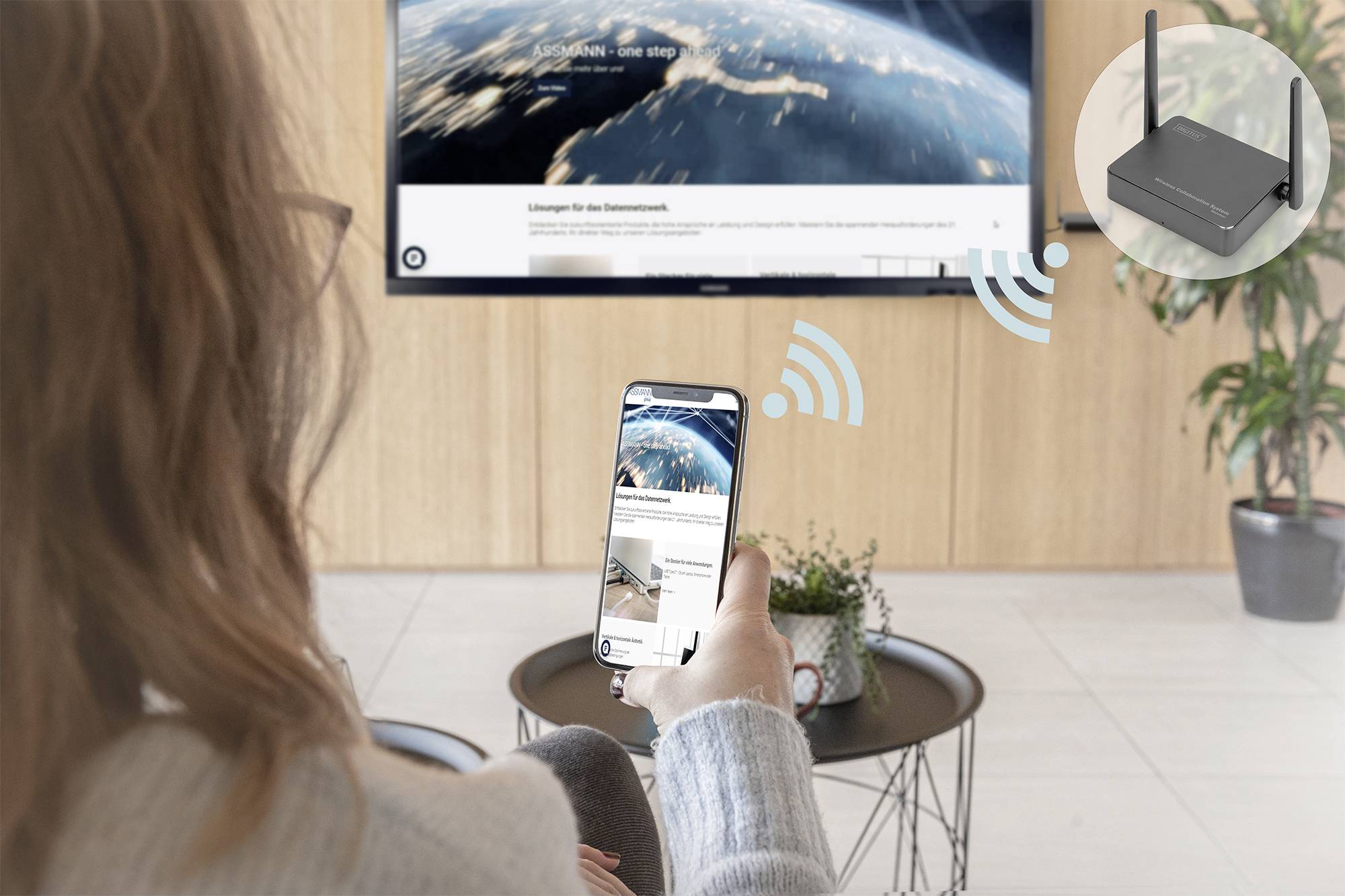 Eine Person nutzt ein Smartphone zur Steuerung eines Smart-TV mit angezeigtem Weltallbild. Ein Symbol zeigt eine WLAN-Verbindung zum Router.