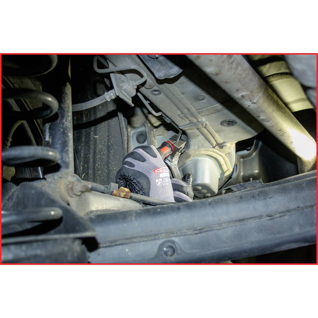Eine Nahaufnahme eines Autoteils mit einem wahrscheinlich reparierenden Handschuh. Metallstrukturen und Mechanik sind sichtbar.