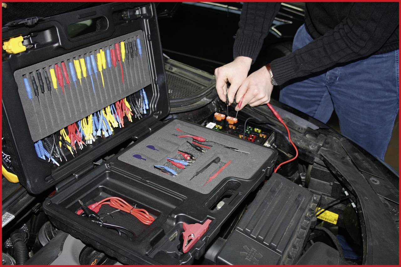 Person arbeitet am offenen Motorraum eines Autos mit Diagnosetools aus einem Werkzeugkoffer. Verschiedene Kabel sind sichtbar.
