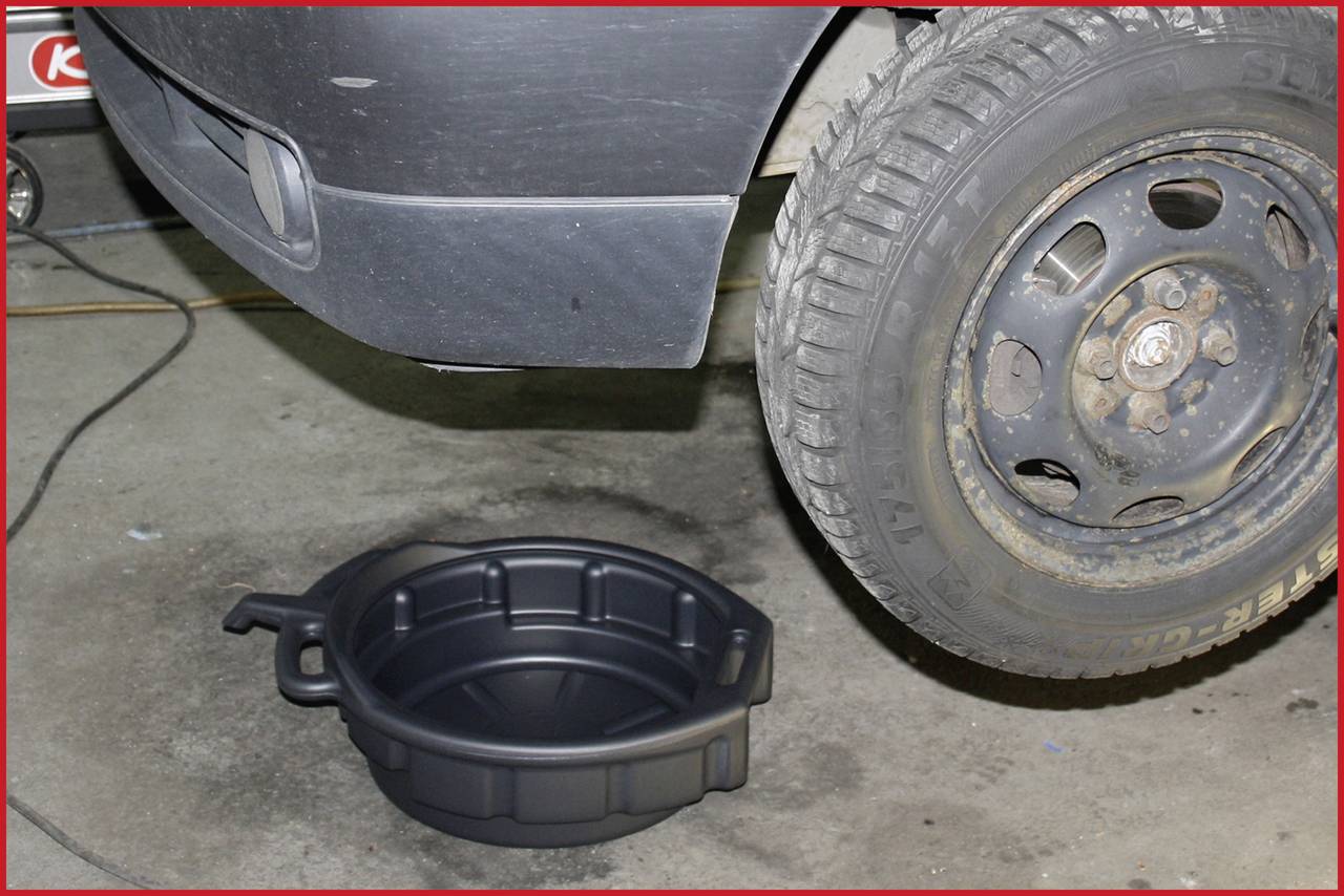 Ein Auto steht aufgebockt, ein Ölauffangbehälter befindet sich darunter zur Vorbereitung auf einen Ölwechsel in einer Werkstatt.