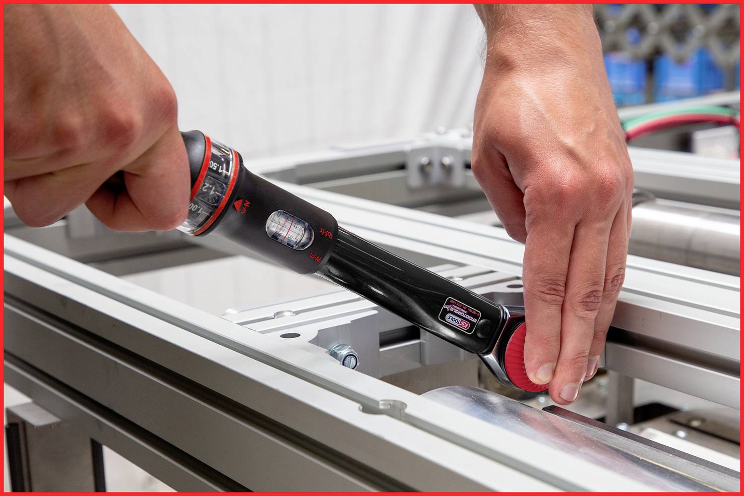 Zwei Hände bedienen ein elektronisches Werkzeug an einer Metallstruktur. Das Werkzeug wird zur Messung oder Justierung verwendet.