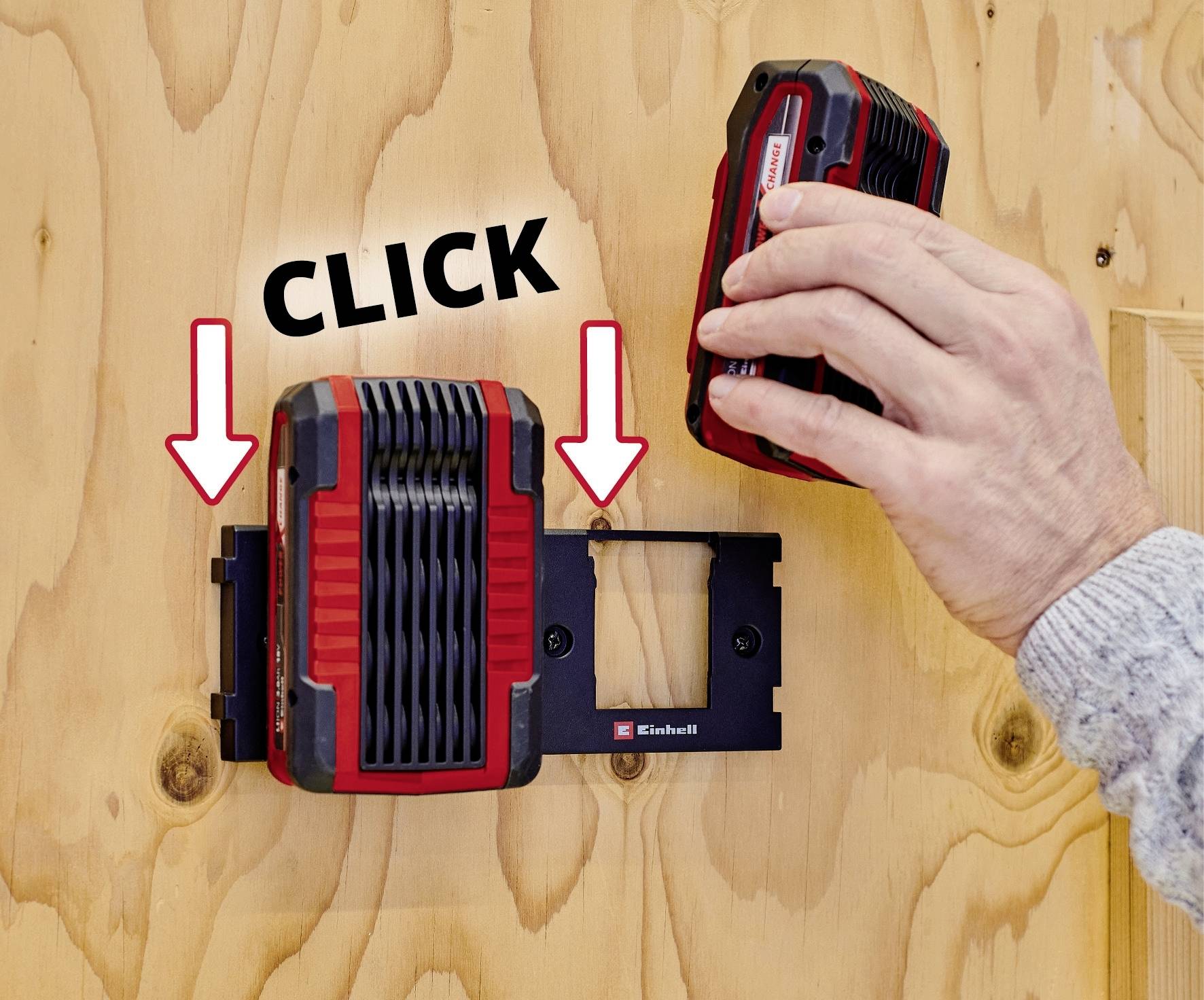 Eine Hand steckt einen roten Akku in ein Ladegerät an der Wand. Zwei Pfeile und das Wort 'CLICK' zeigen die Einsteckrichtung.
