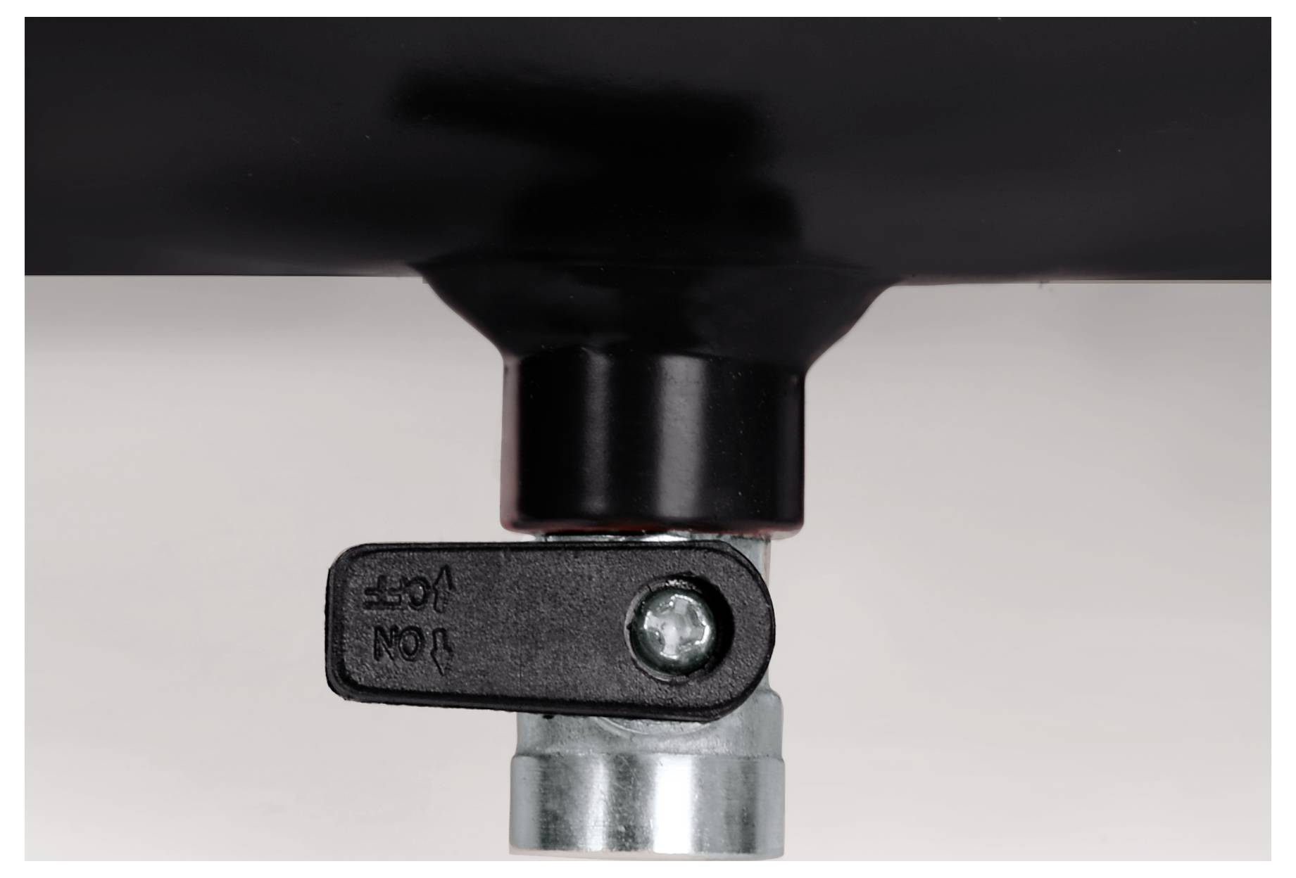 Nahaufnahme eines schwarzen Kunststoffhebelventils, das an einem Metallrohr oder einer Metallfitting gegen einen schlichten Hintergrund angebracht ist.