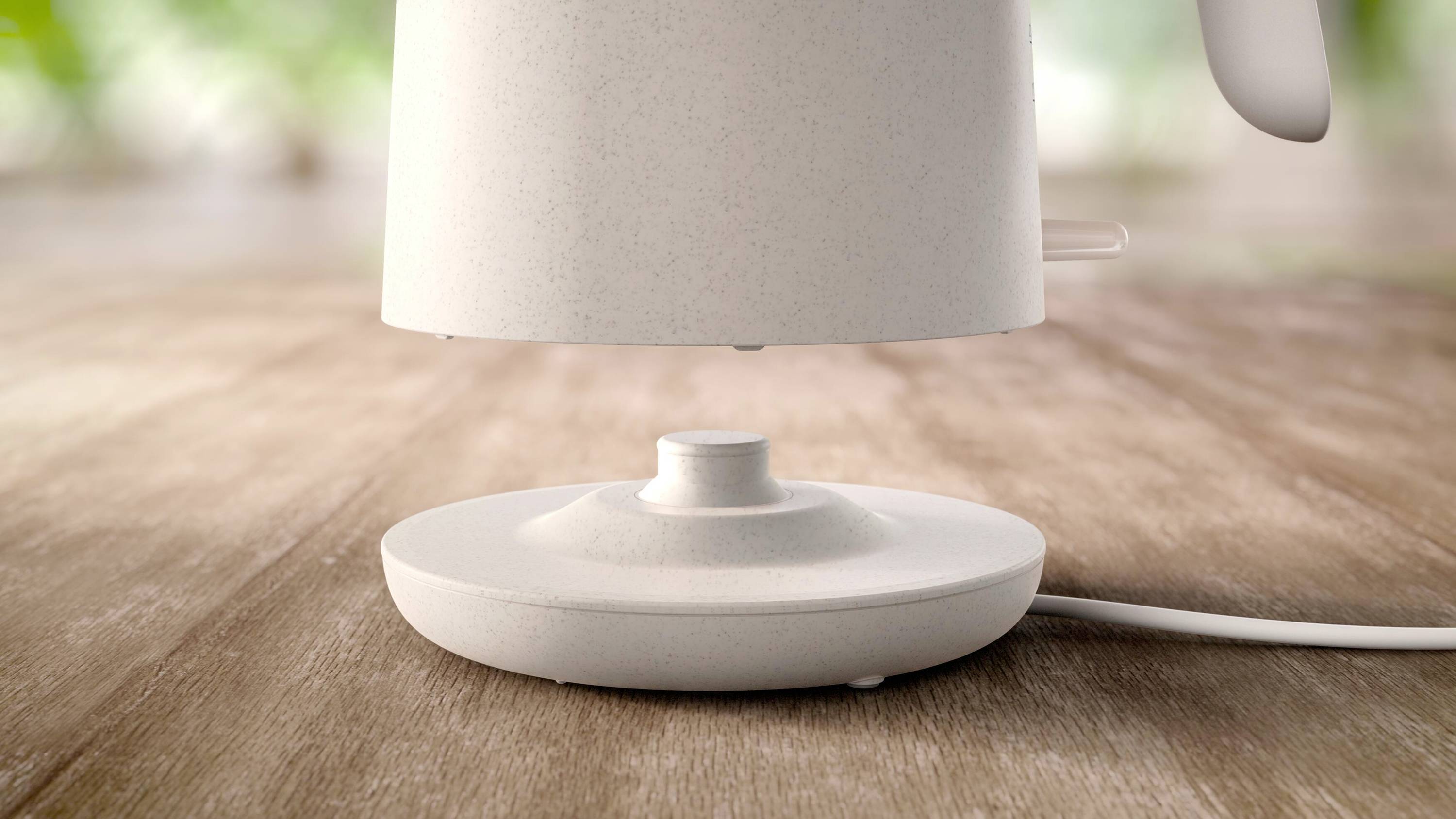 Ein weißer Wasserkocher schwebt über seiner Basis auf einem Holztisch. Im Hintergrund sind verschwommene, grüne Pflanzen erkennbar.