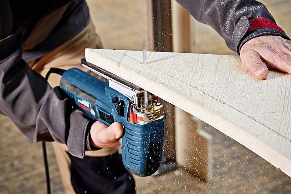 Eine Person sägt ein Stück Holz mit einer elektrischen Stichsäge. Holzspäne fliegen umher.