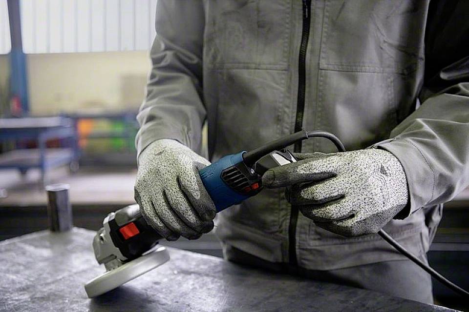 Eine Person in Arbeitskleidung hält eine elektrische Schleifmaschine in der Hand, bereit zur Benutzung in einer Werkstattumgebung.